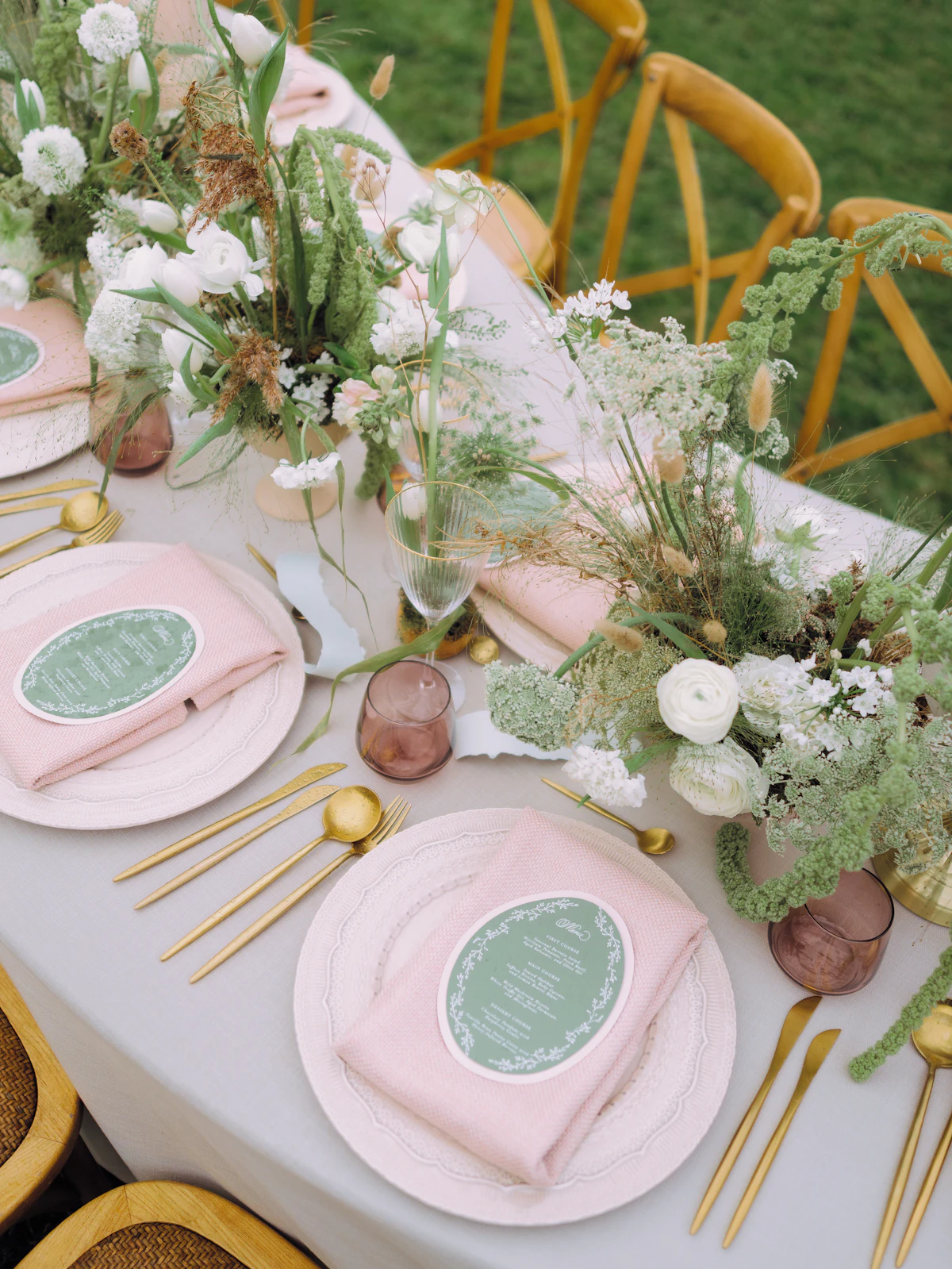 Pink napkins, gold cutlery and green menu cards on a wedding table decorated with white flowers