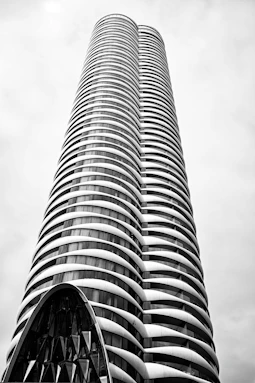 Modern skyscraper with curved balconies against a cloudy sky.