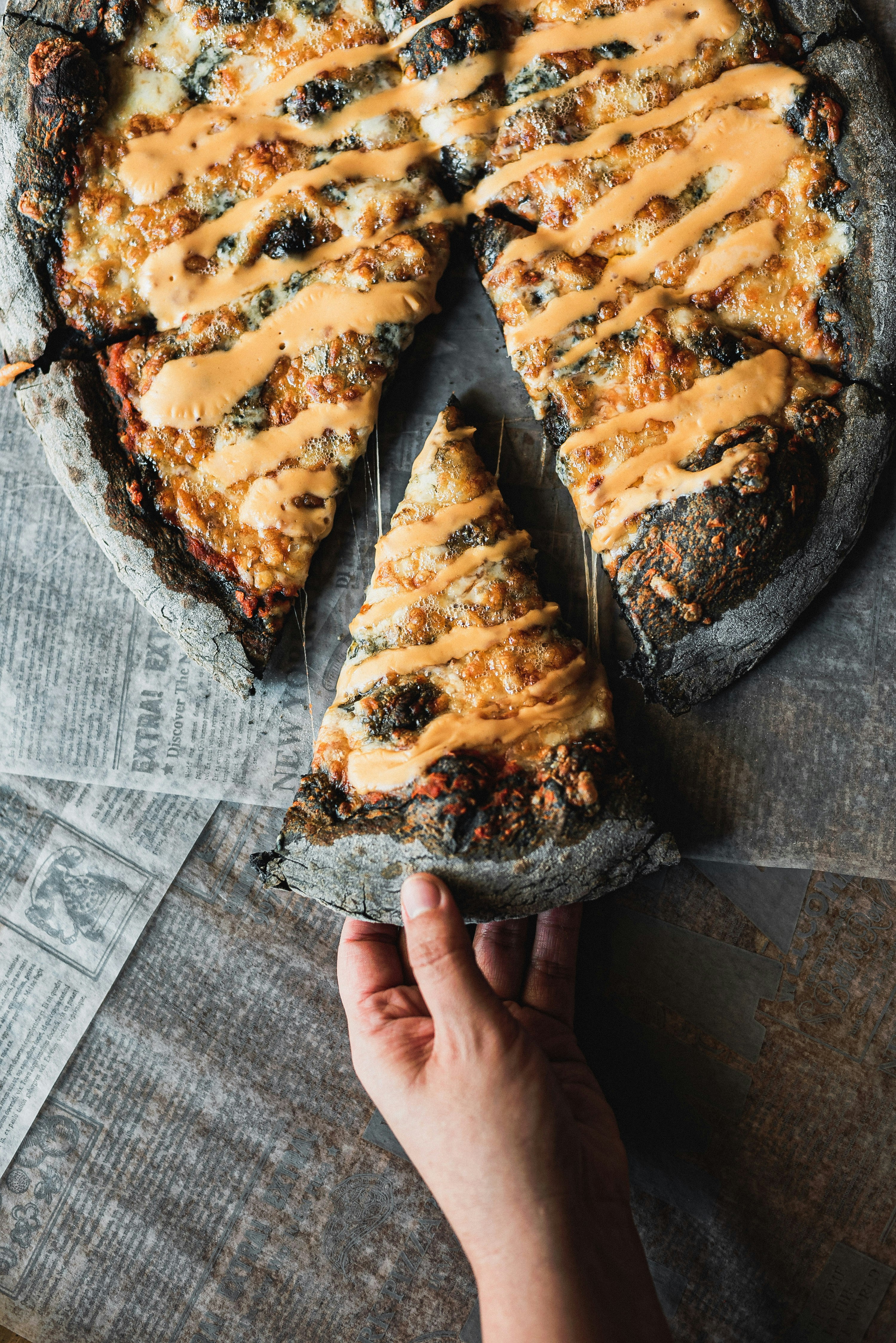 A hand holds a slice of black crust pizza.