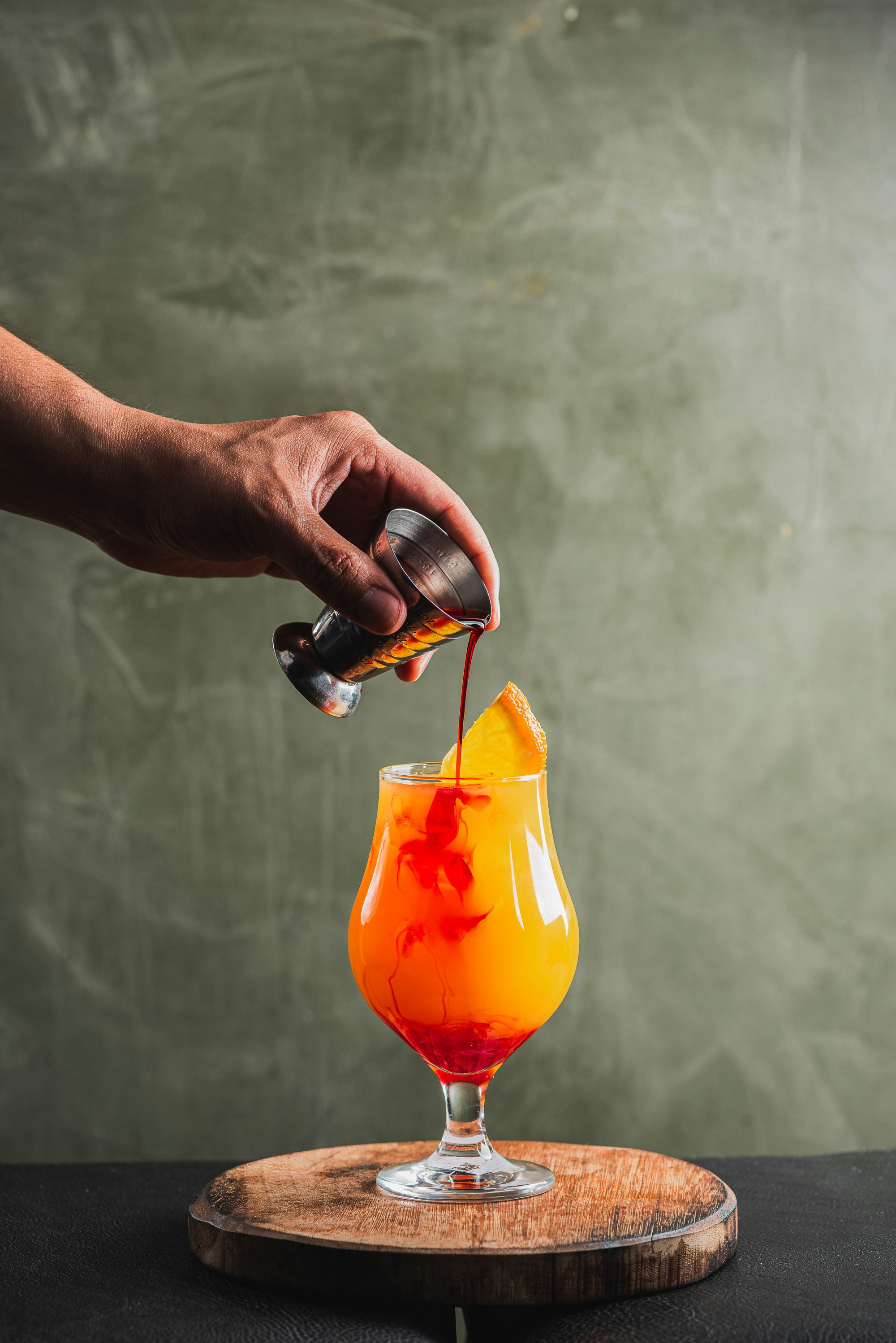 Bartender pouring a colorful cocktail with orange garnish
