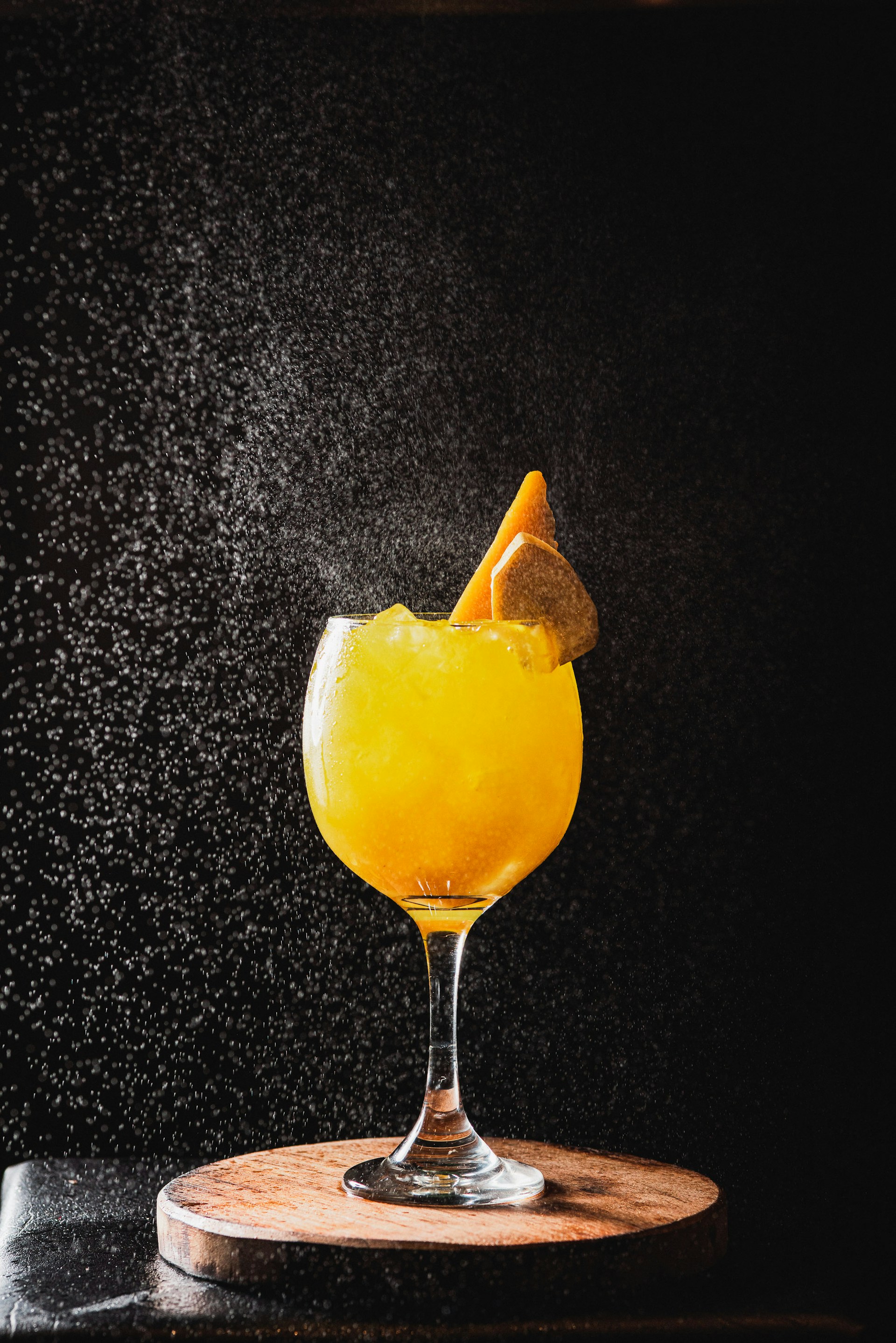 A bright yellow cocktail with ice and fruit garnish.