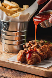 Sauce being poured on fried chicken lollipops and fries.