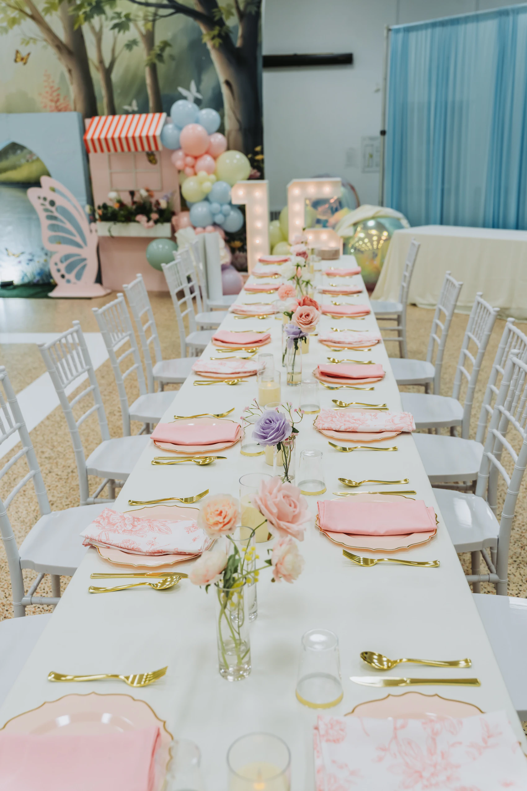 Long celebration table styled with pink decorations, florals, and balloons