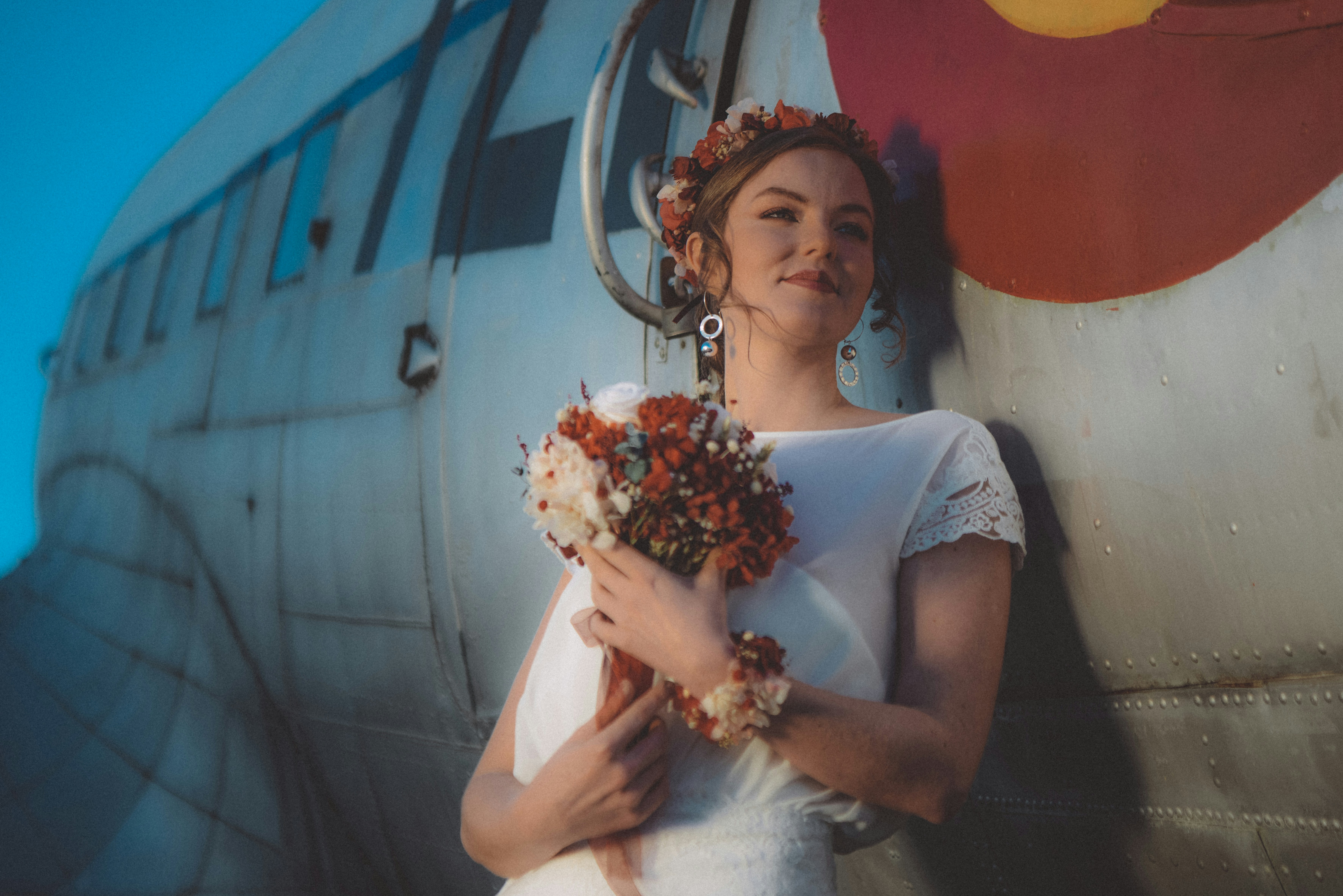 Woman in white dress holding flowers by airplane