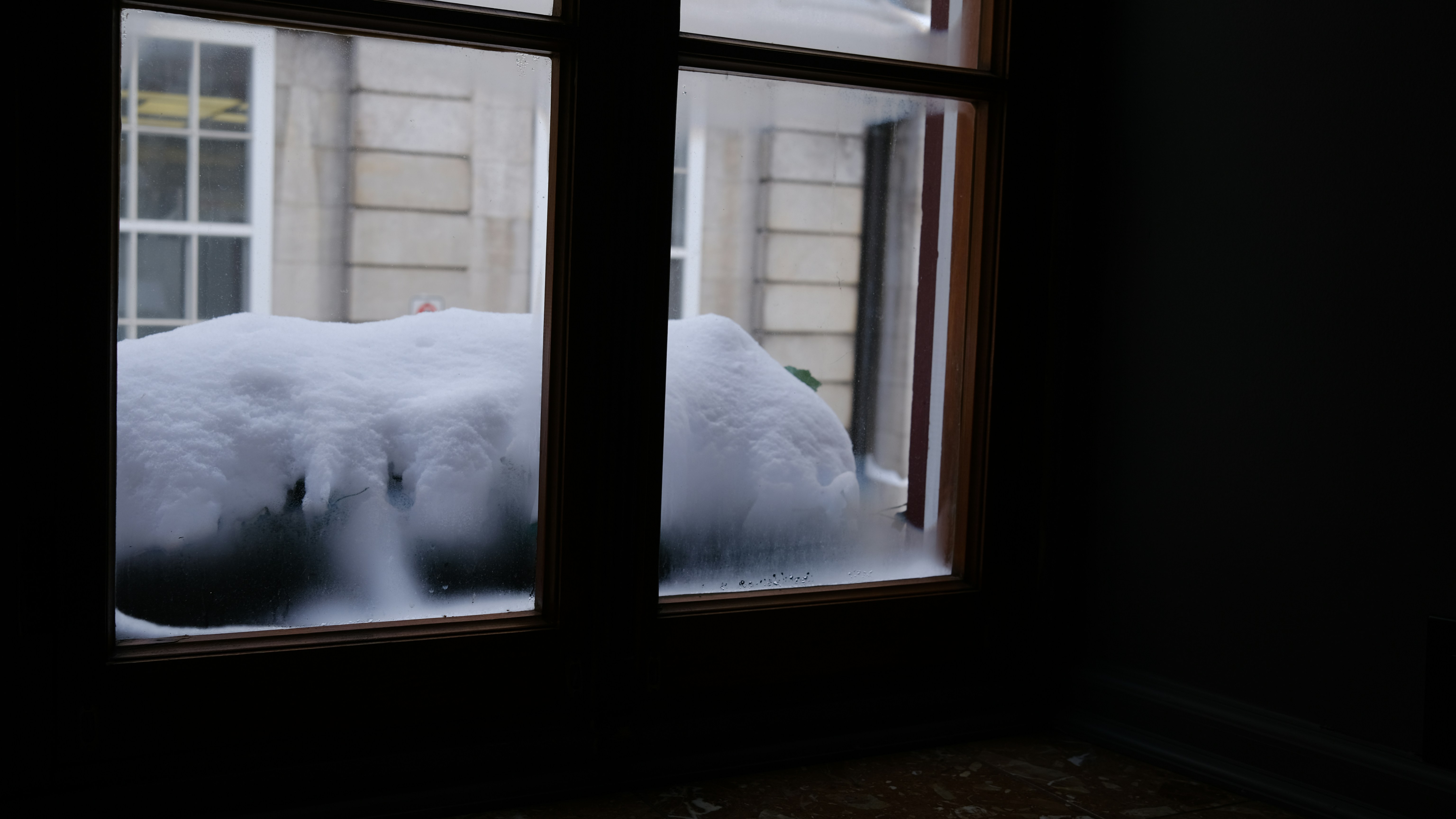 Thick snow drifts outside a window pane.