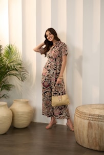 A smiling woman in a floral jumpsuit holds a purse.