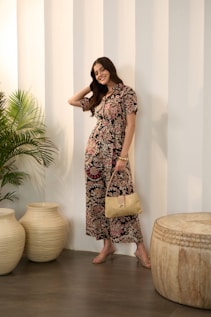 A smiling woman in a floral jumpsuit holds a purse.