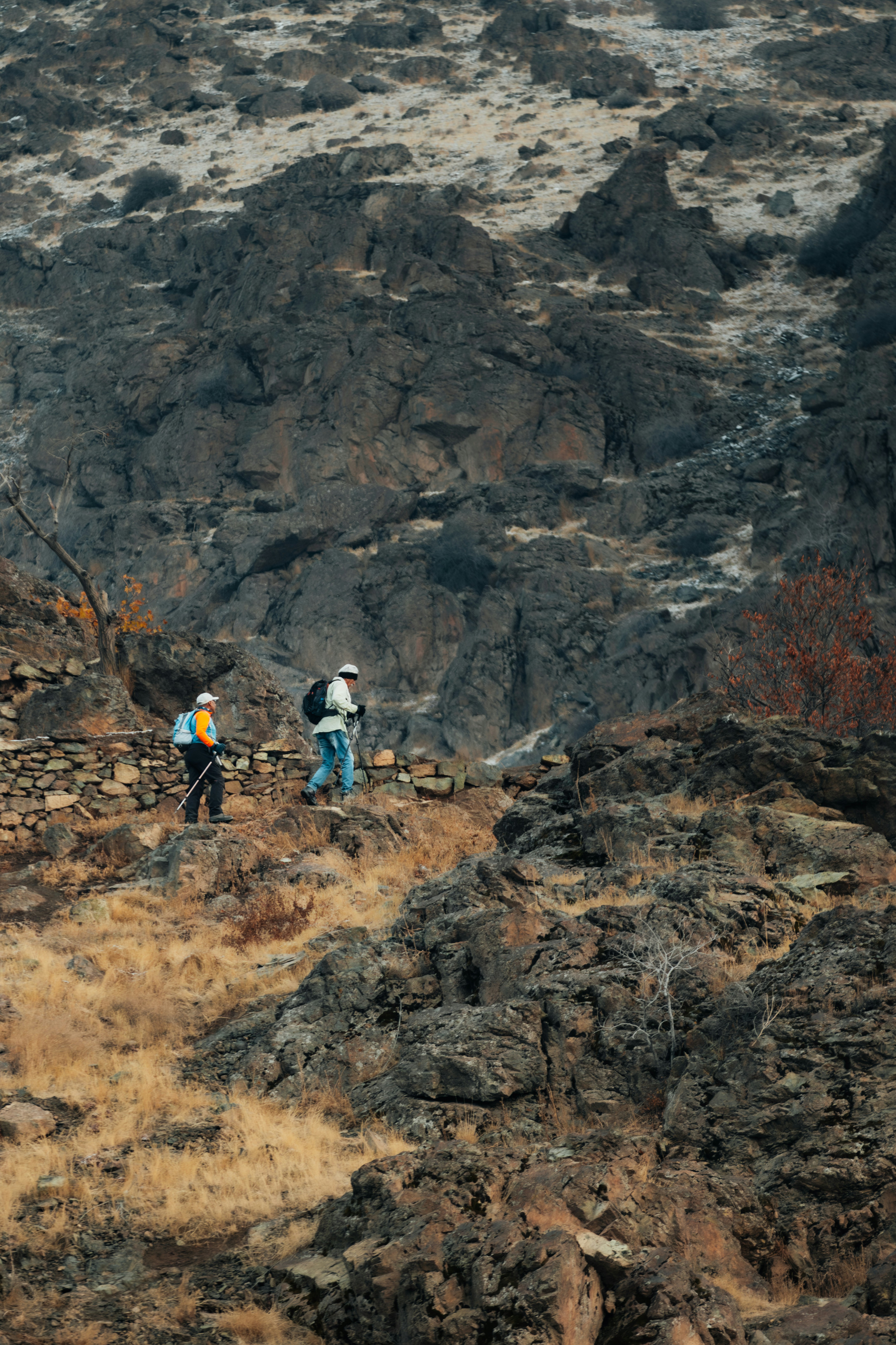 Two hikers ascend a rocky, barren mountain trail.