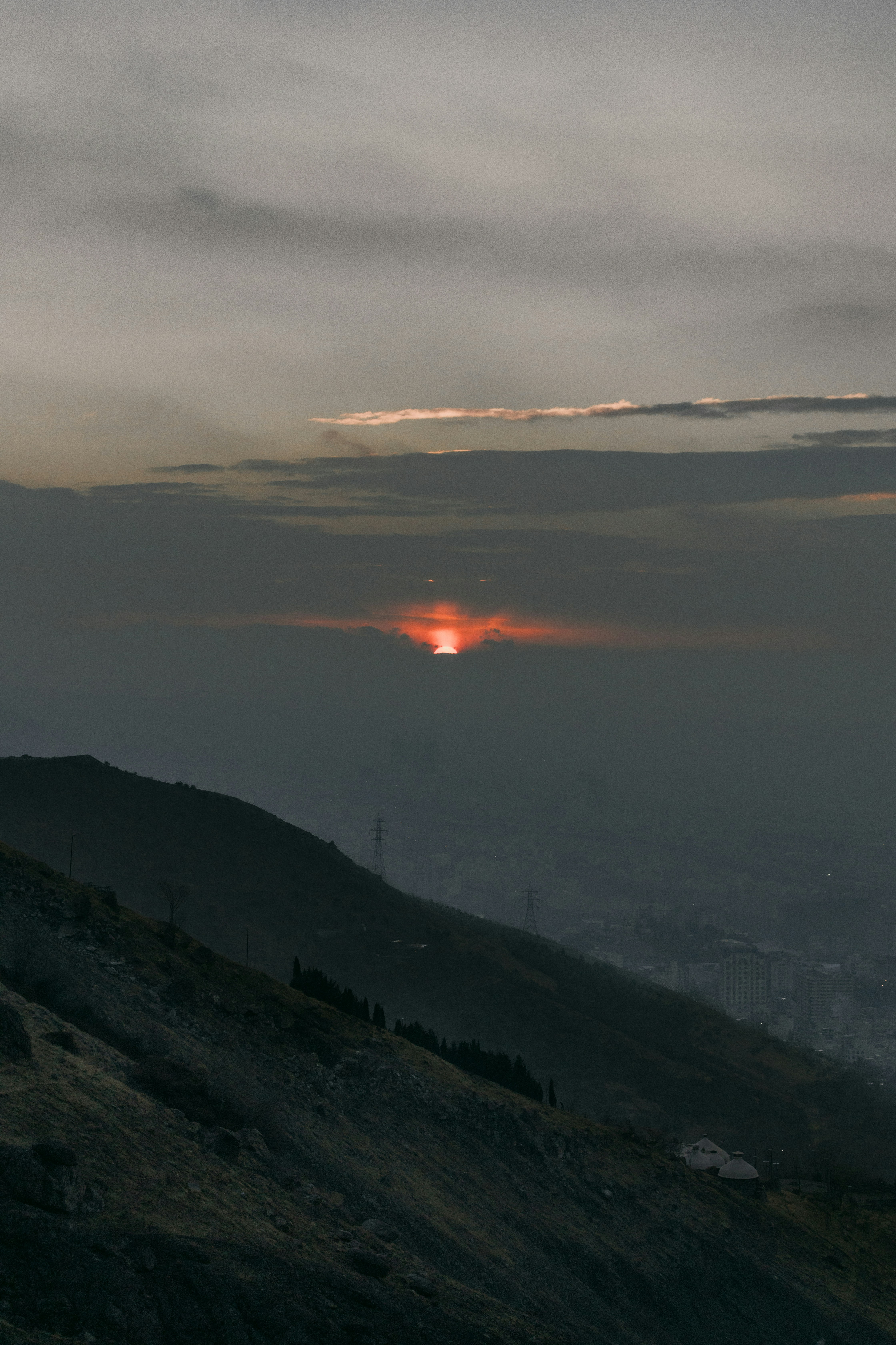 Sunset behind clouds over a hazy city skyline.