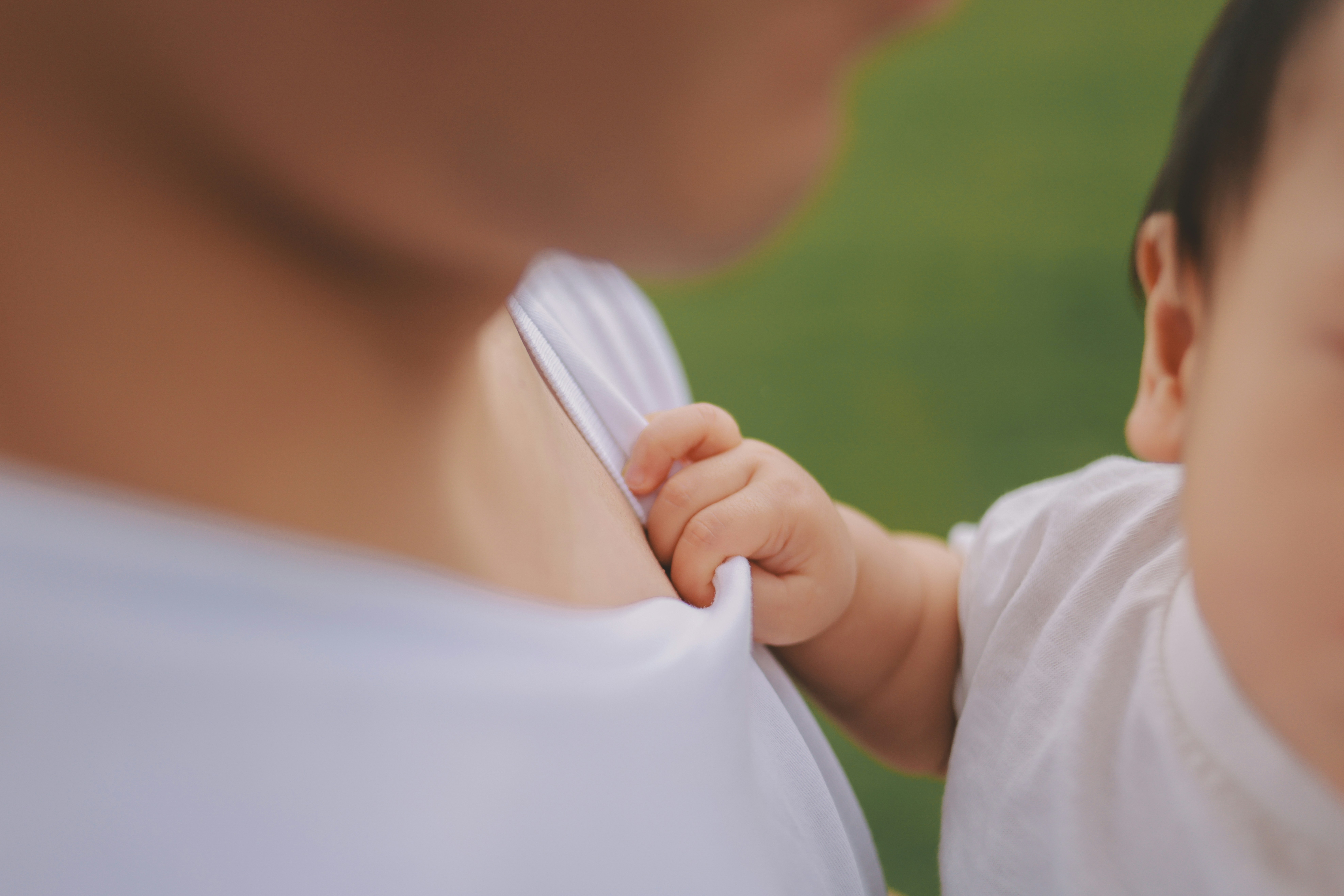 Baby's hand holding parent's shirt with green background