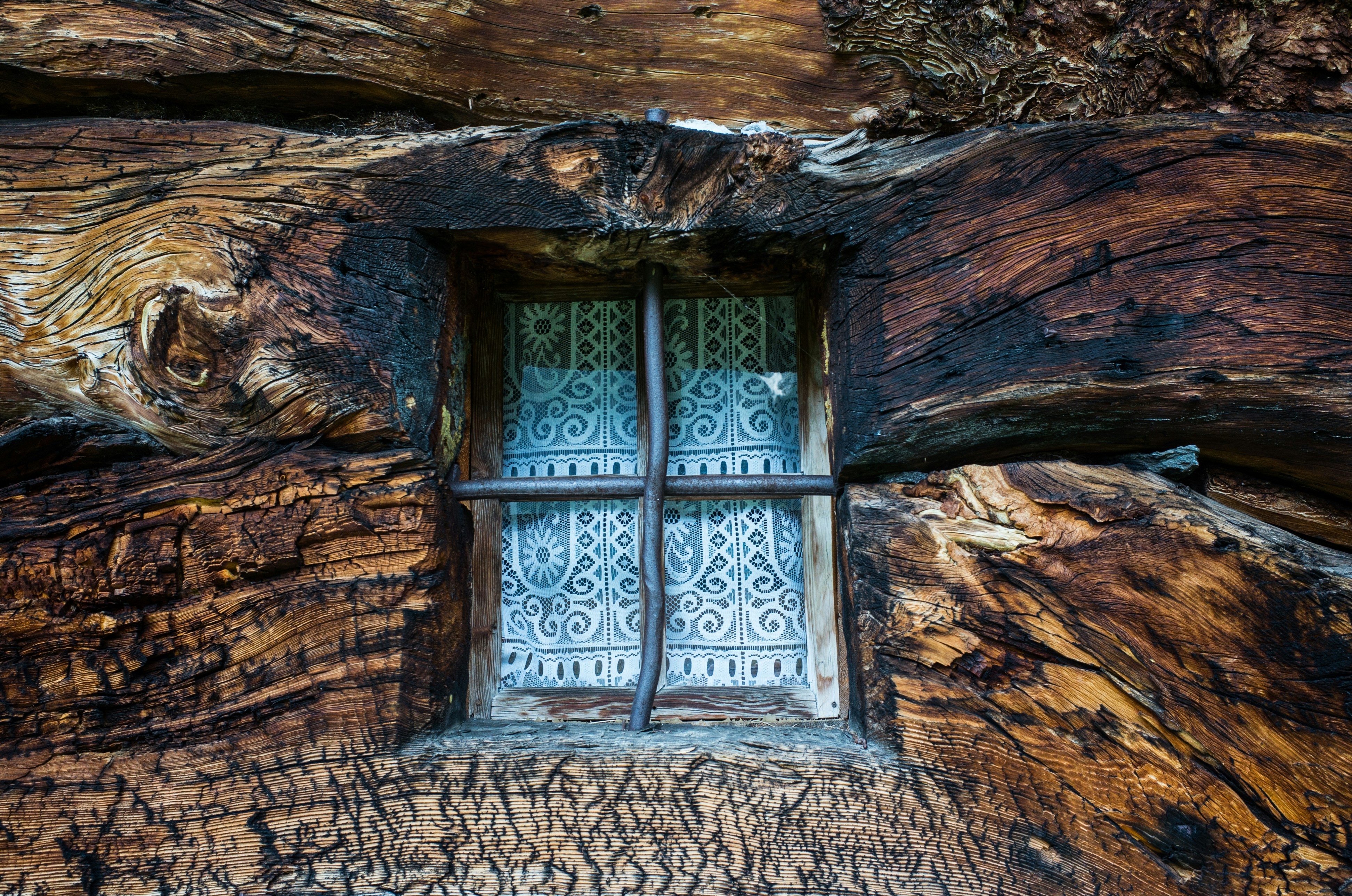 Rustic wooden cabin window with intricate white curtains.