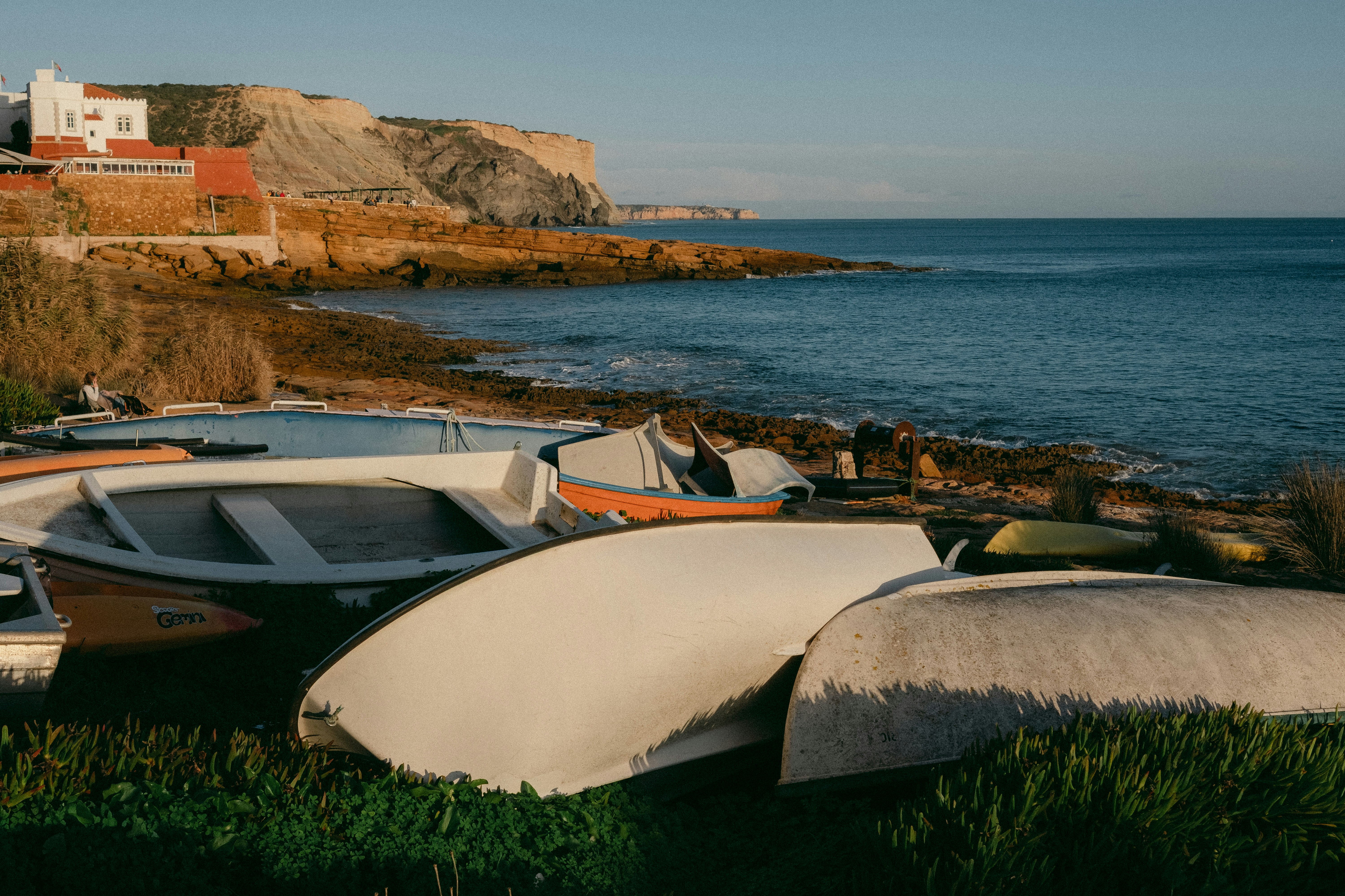 Several boats resting on a grassy shore near the ocean.