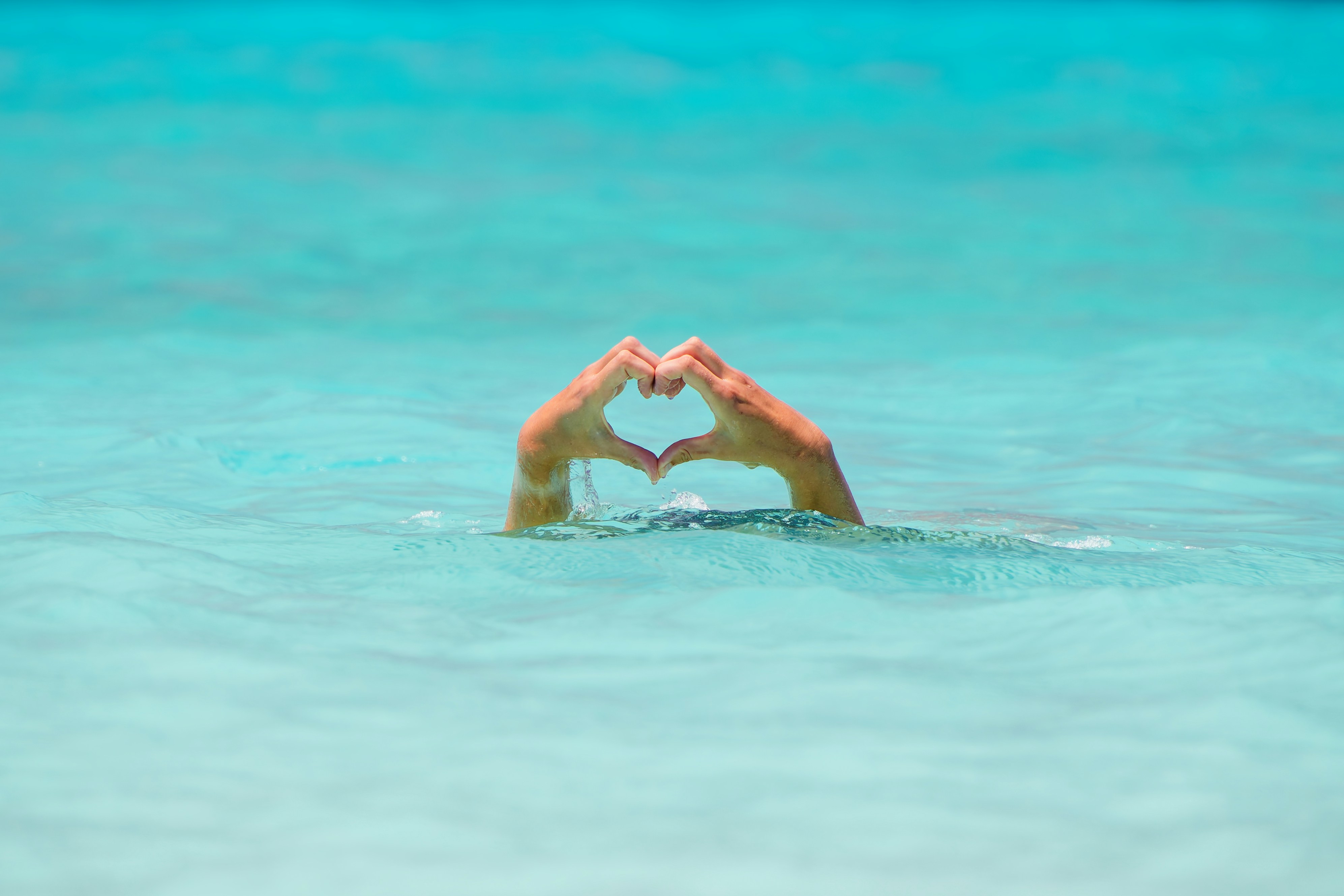 Hands forming a heart shape in clear ocean water.