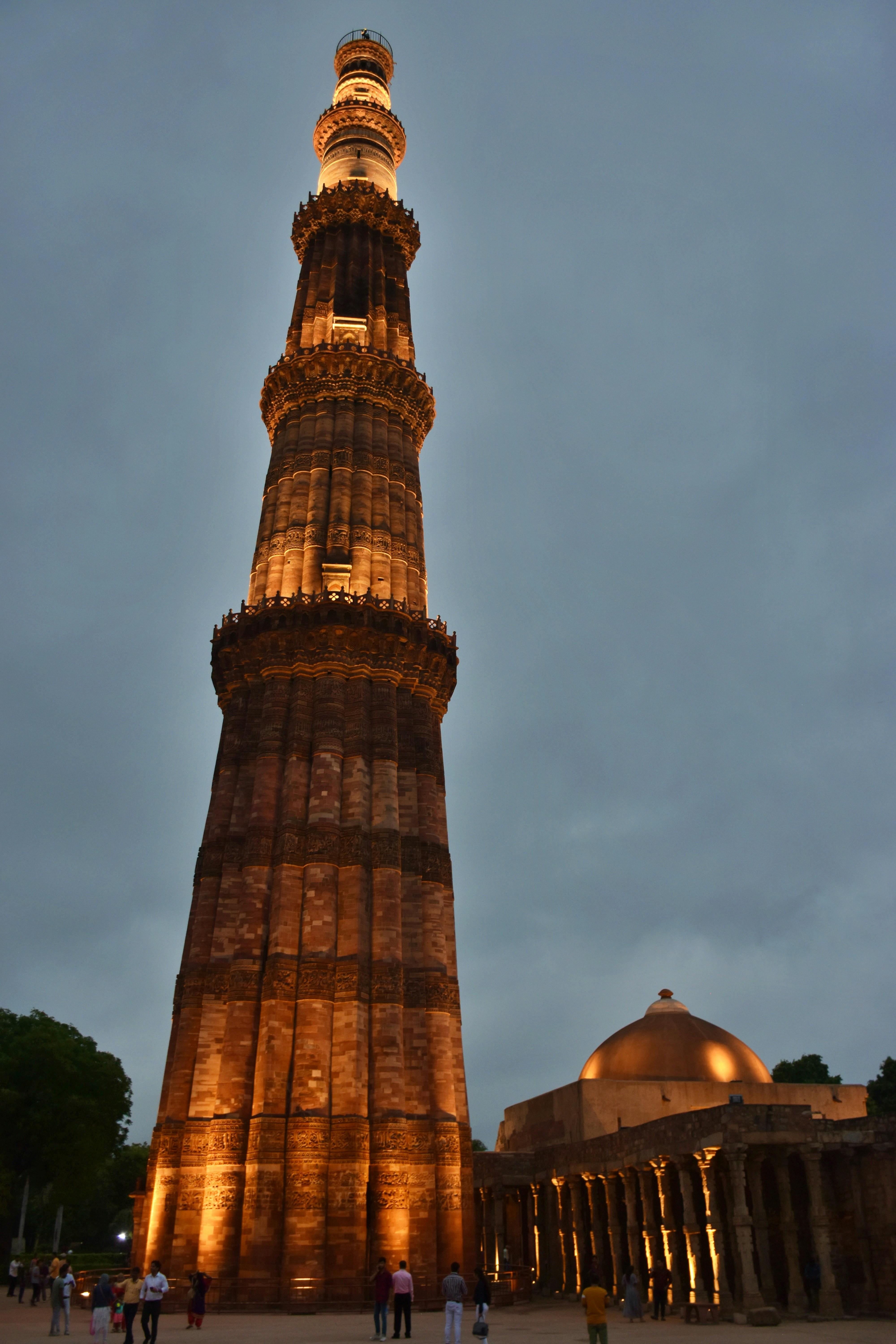 Qutub minar tower illuminated at dusk with a dome structure.