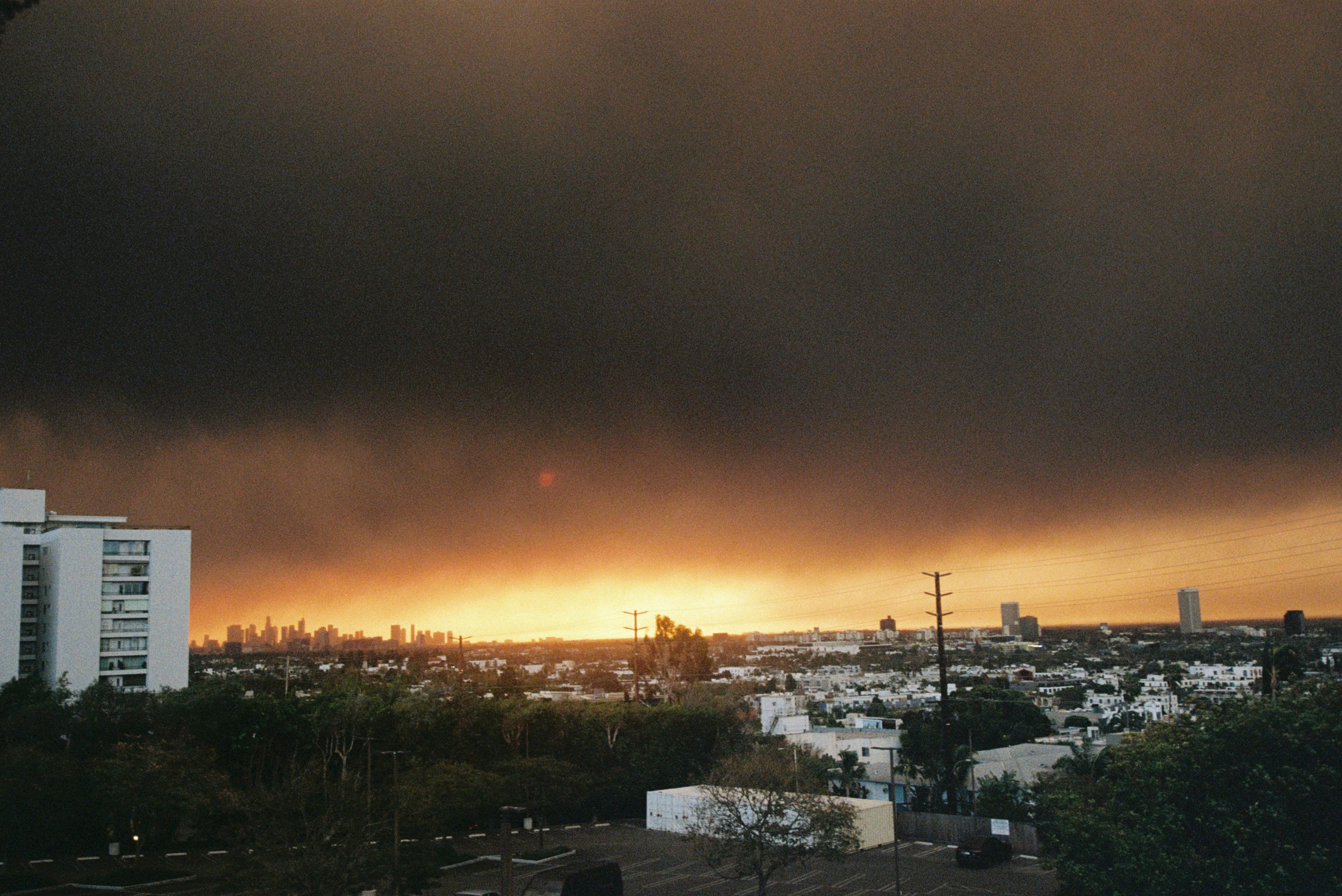Dark clouds obscure a vibrant sunset over city buildings.