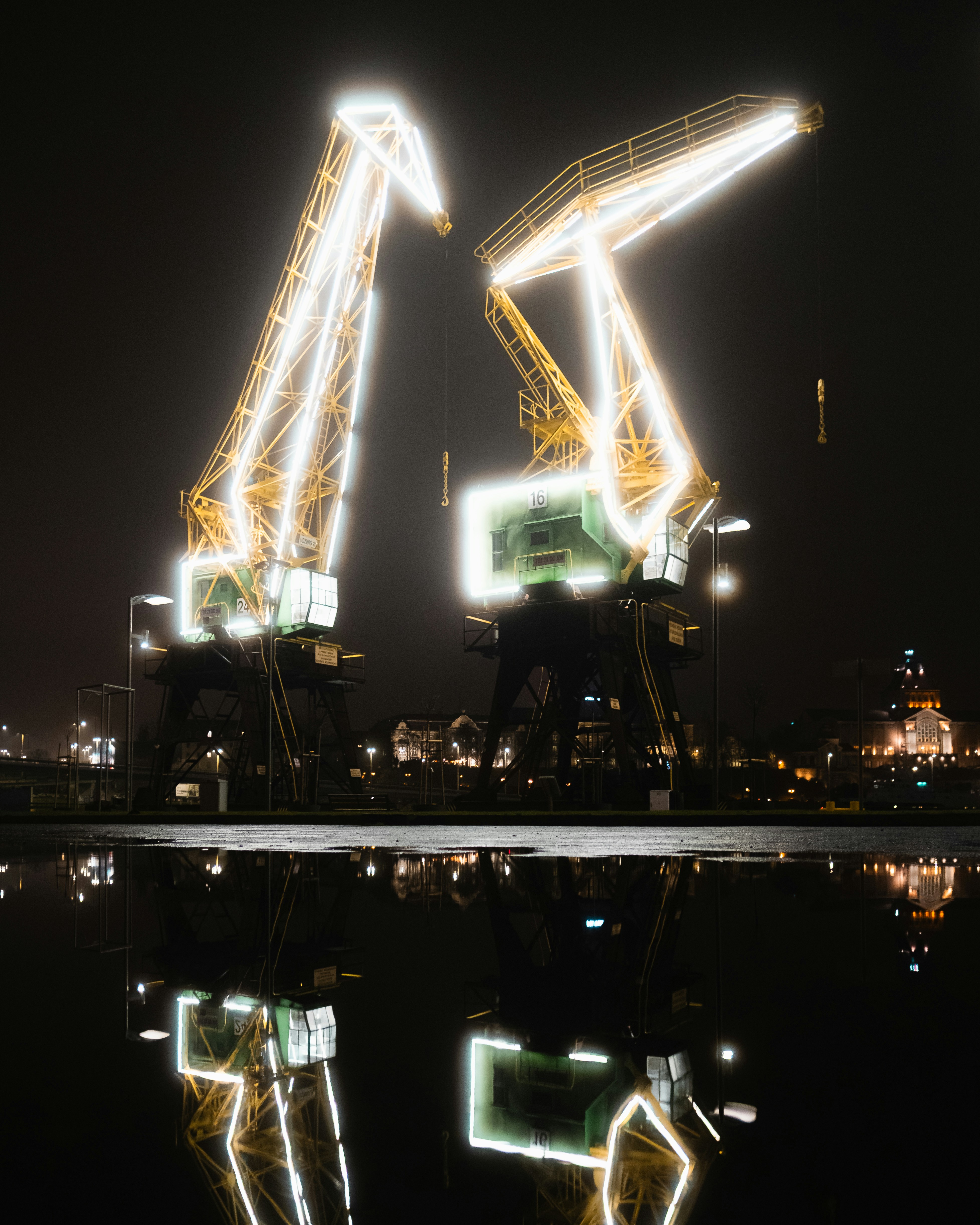 Dos grúas iluminadas por la noche reflejadas en el agua.