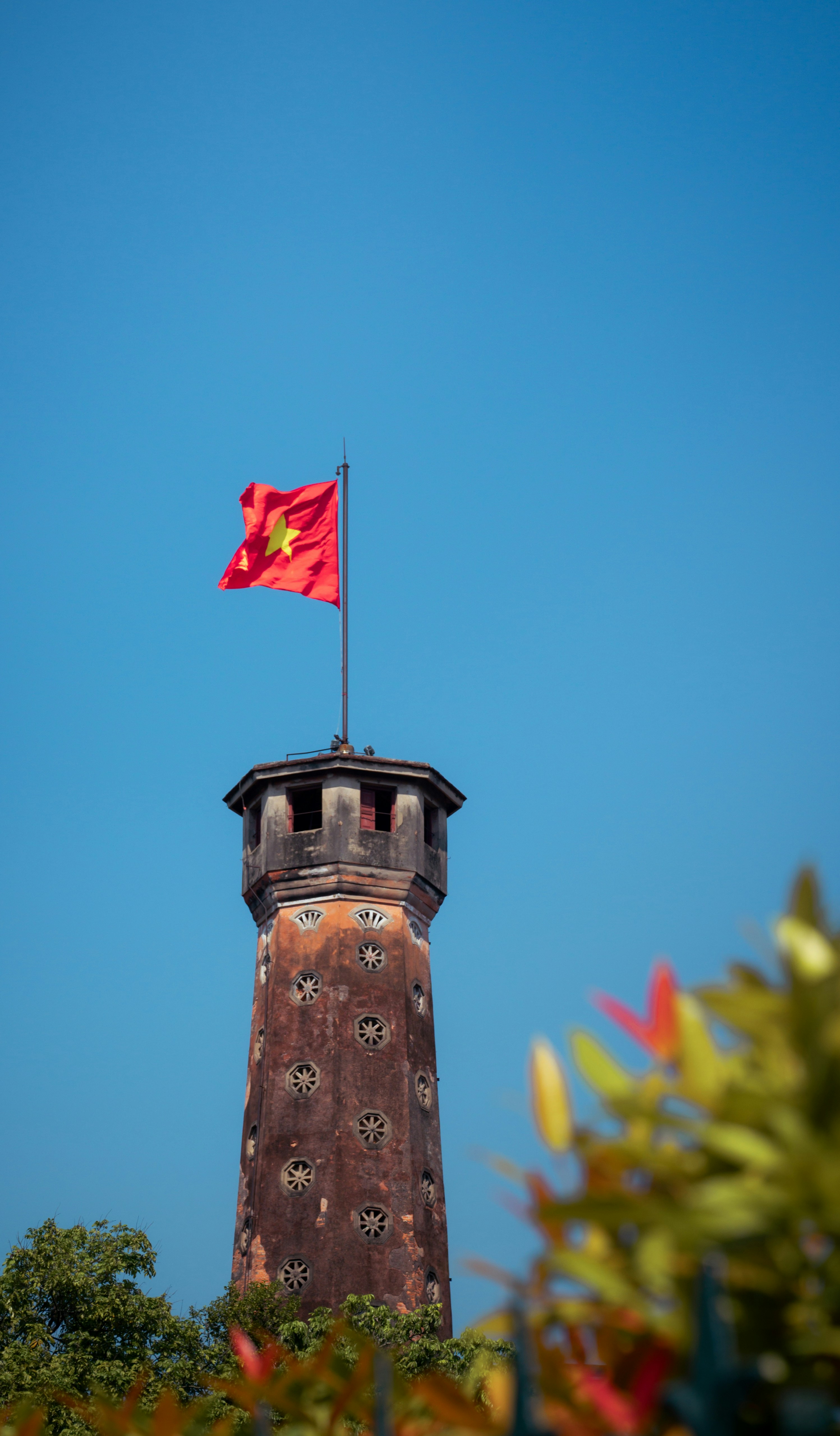 A vietnamese flag flies atop a historic tower.