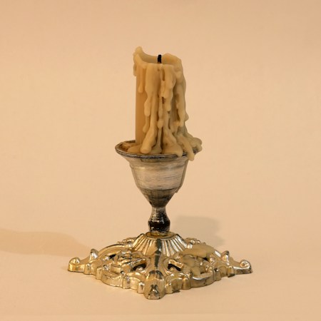 Melted candle in an ornate silver candlestick, similar to the taper candles guests will decorate at Henderson's new Spell Candle Carving Workshop
