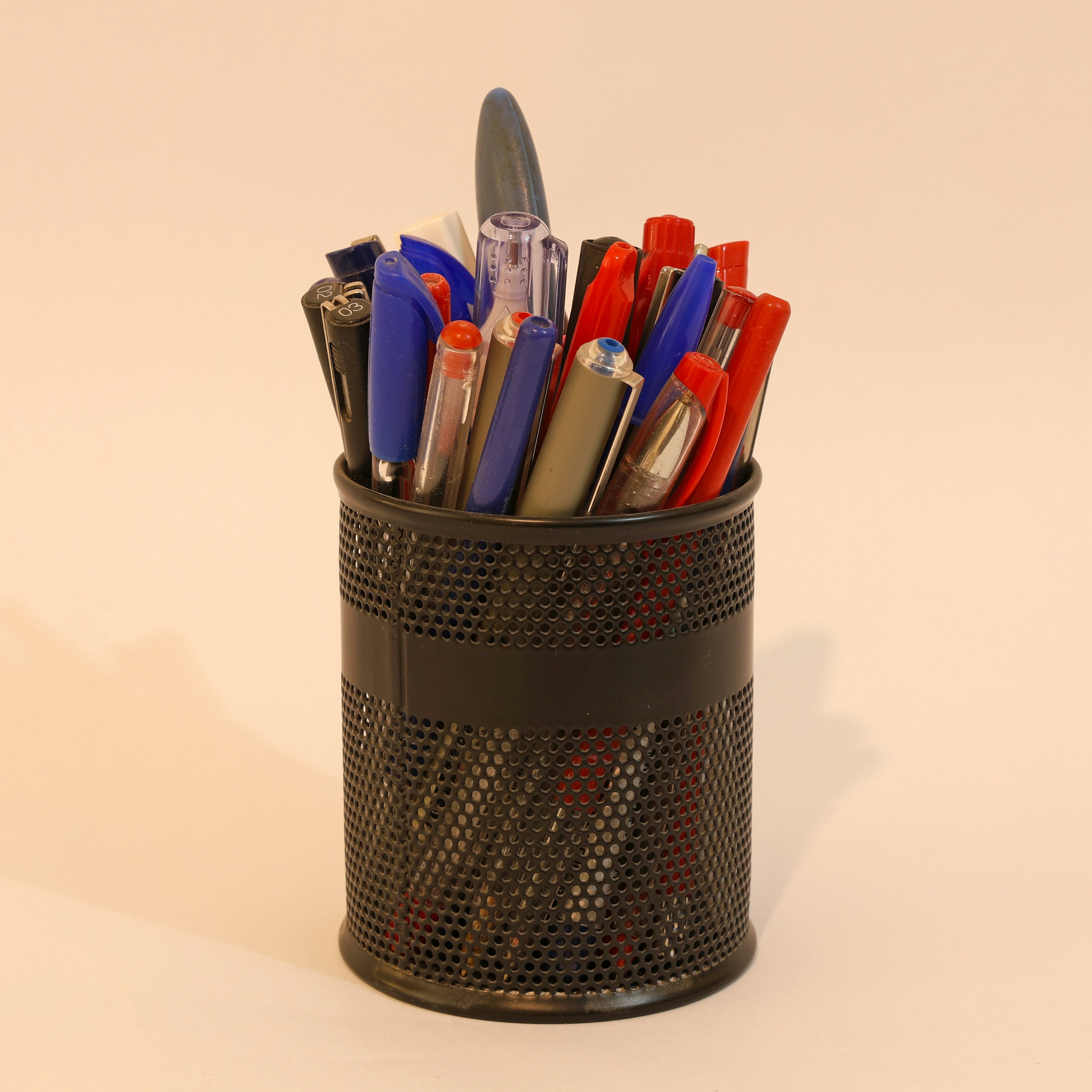 A metal cup filled with assorted pens and pencils.