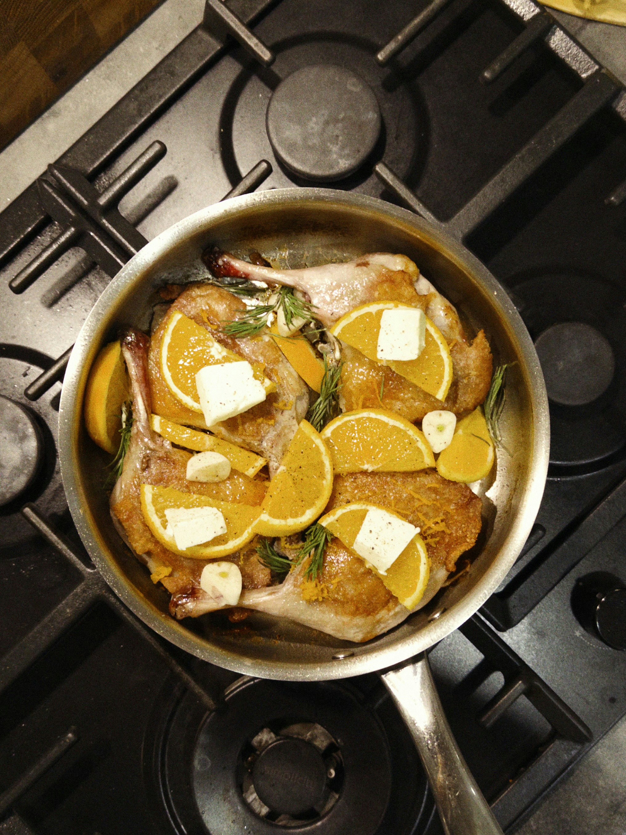 Duck confit with orange slices and butter in pan.