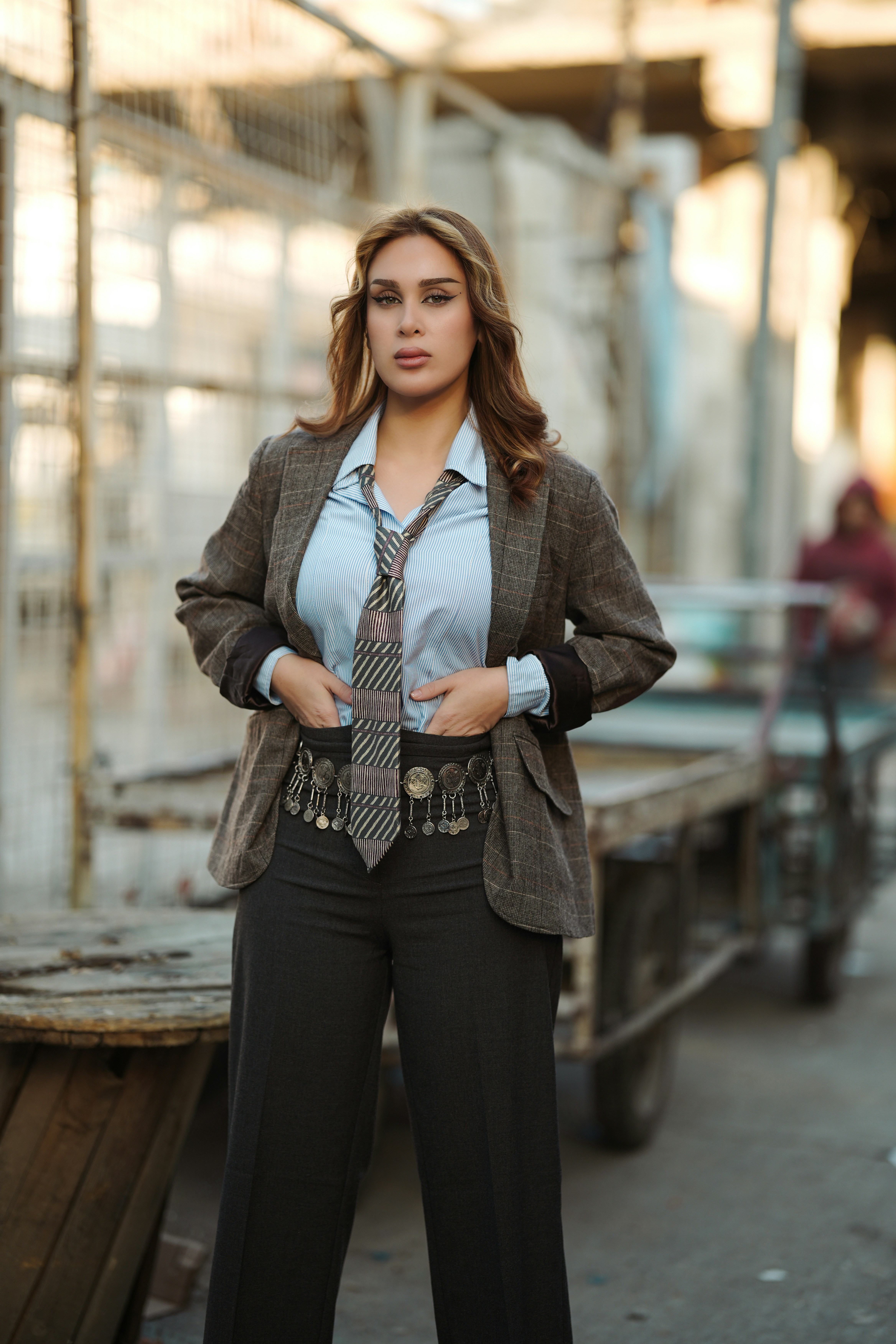 Woman in blazer and tie stands with hands in pockets.