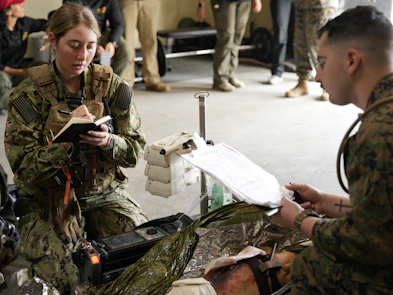 Two marines practice medical procedures with equipment