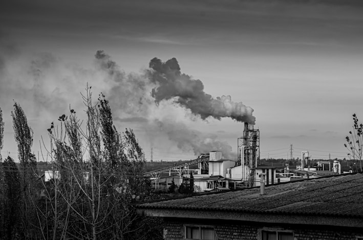Industrial factory emitting smoke against a cloudy sky.
