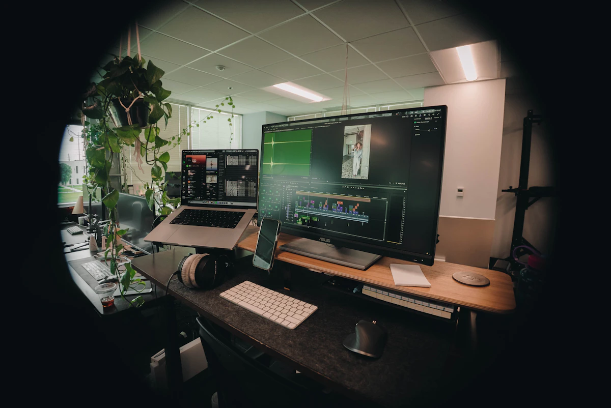 Computer workstation with multiple monitors and plants.