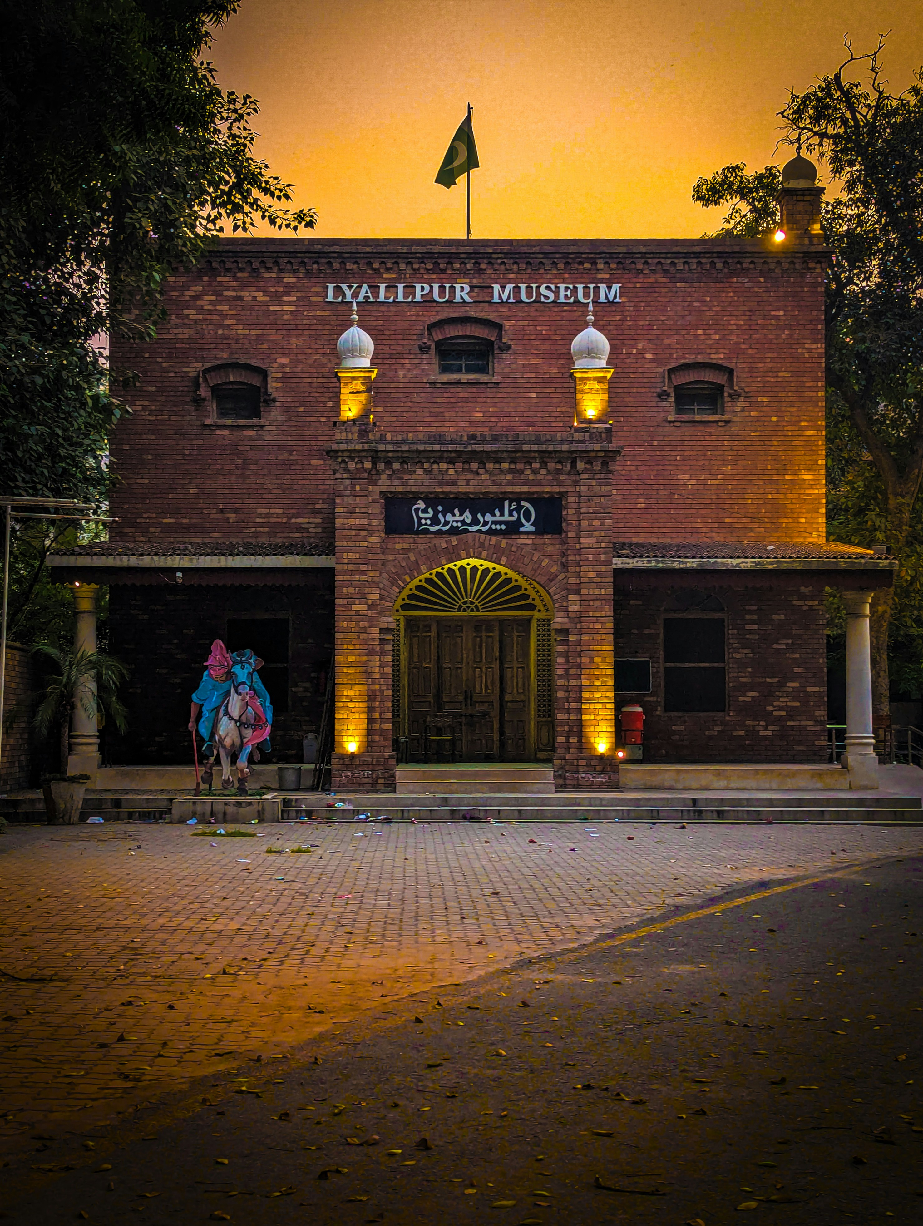 Bangunan museum Lyallpur saat matahari terbenam dengan orang-orang dan kuda.