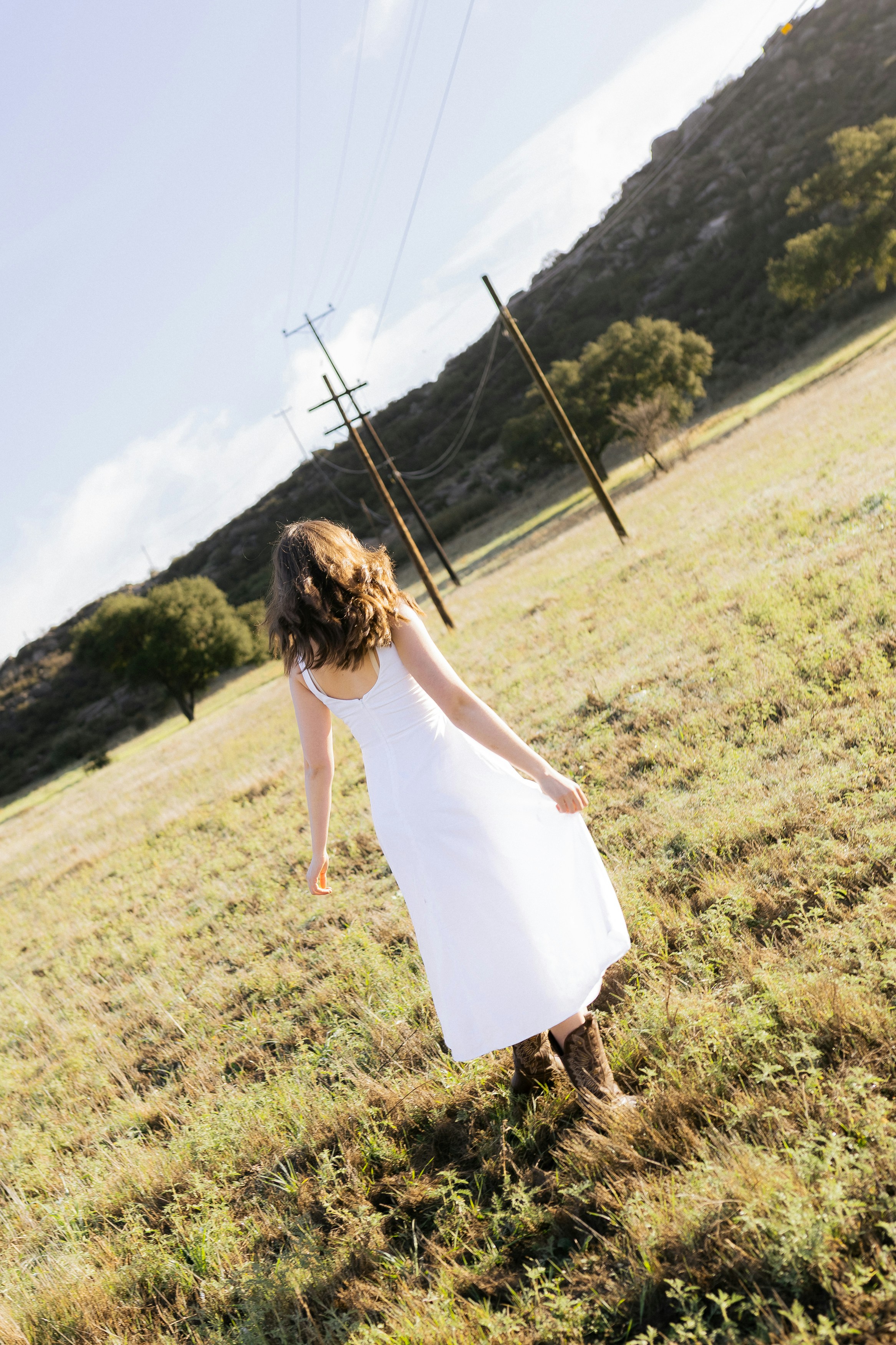 Woman in white dress walks through a grassy field.