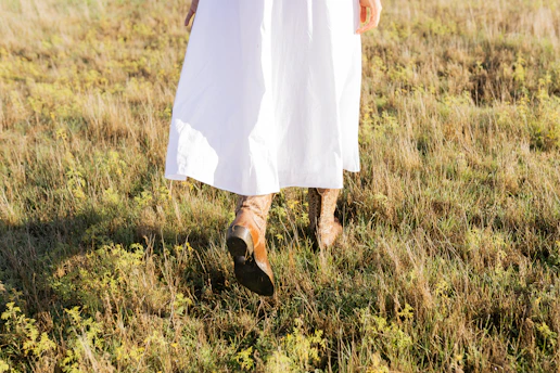 Woman in white dress walks through grassy field