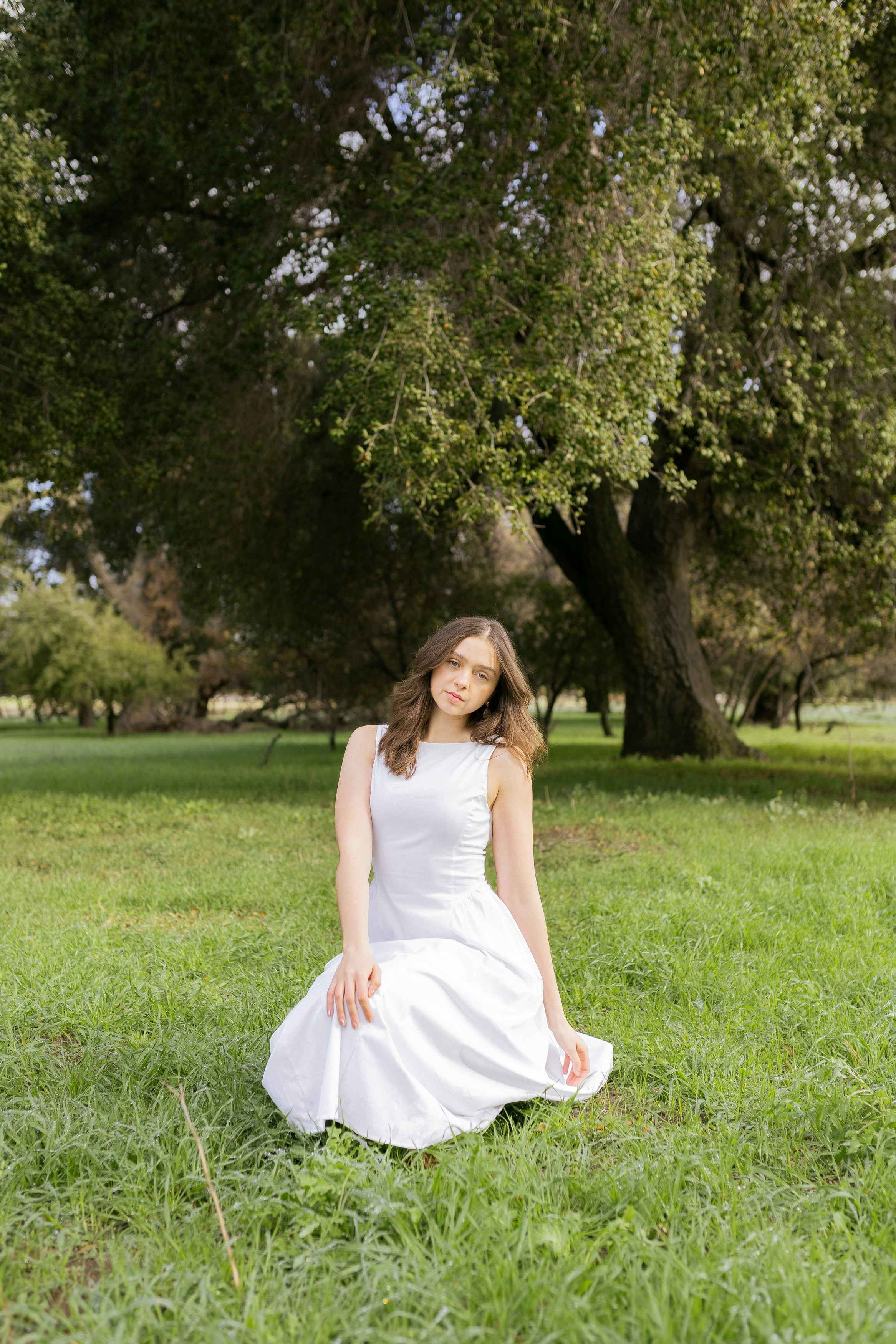 Young woman in white dress sitting in grassy field