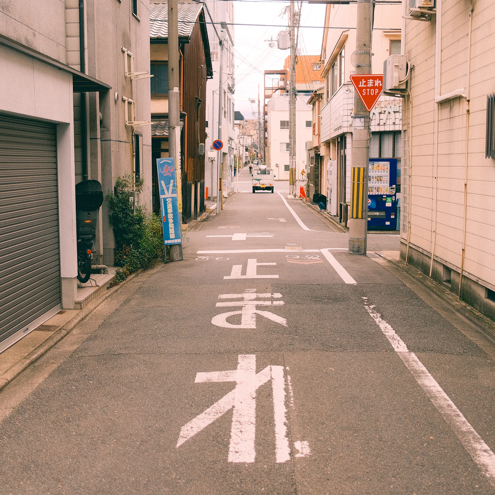 A narrow street in Kyoto has a Japanese stop sign beside a parked car