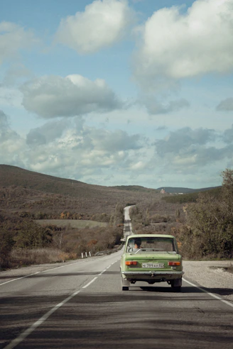 A green car drives down a long, winding road.