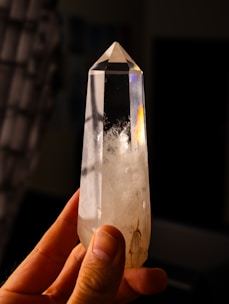Hand holding a clear quartz crystal with inclusions.