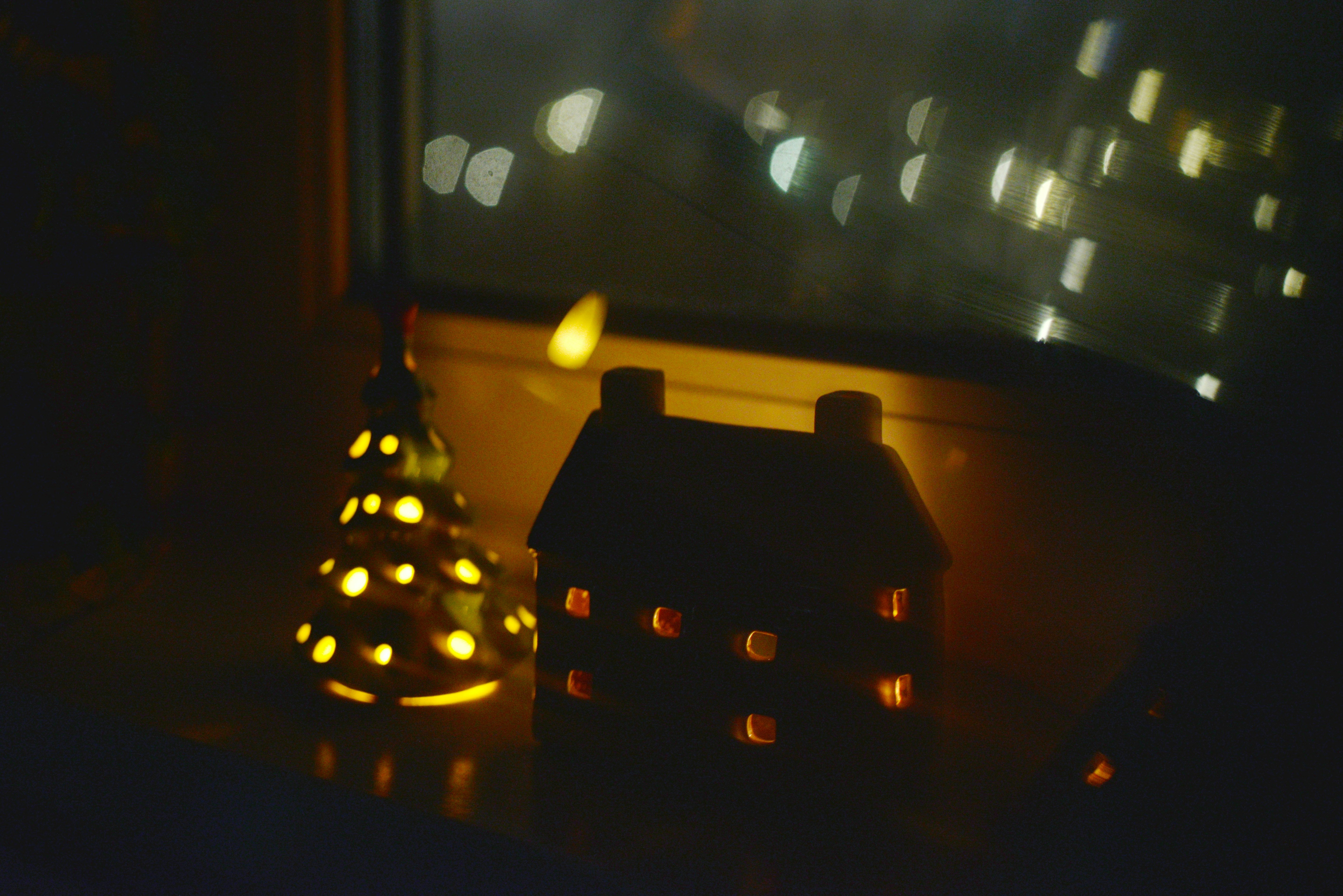 Duas decorações natalinas de cerâmica iluminadas no parapeito da janela.