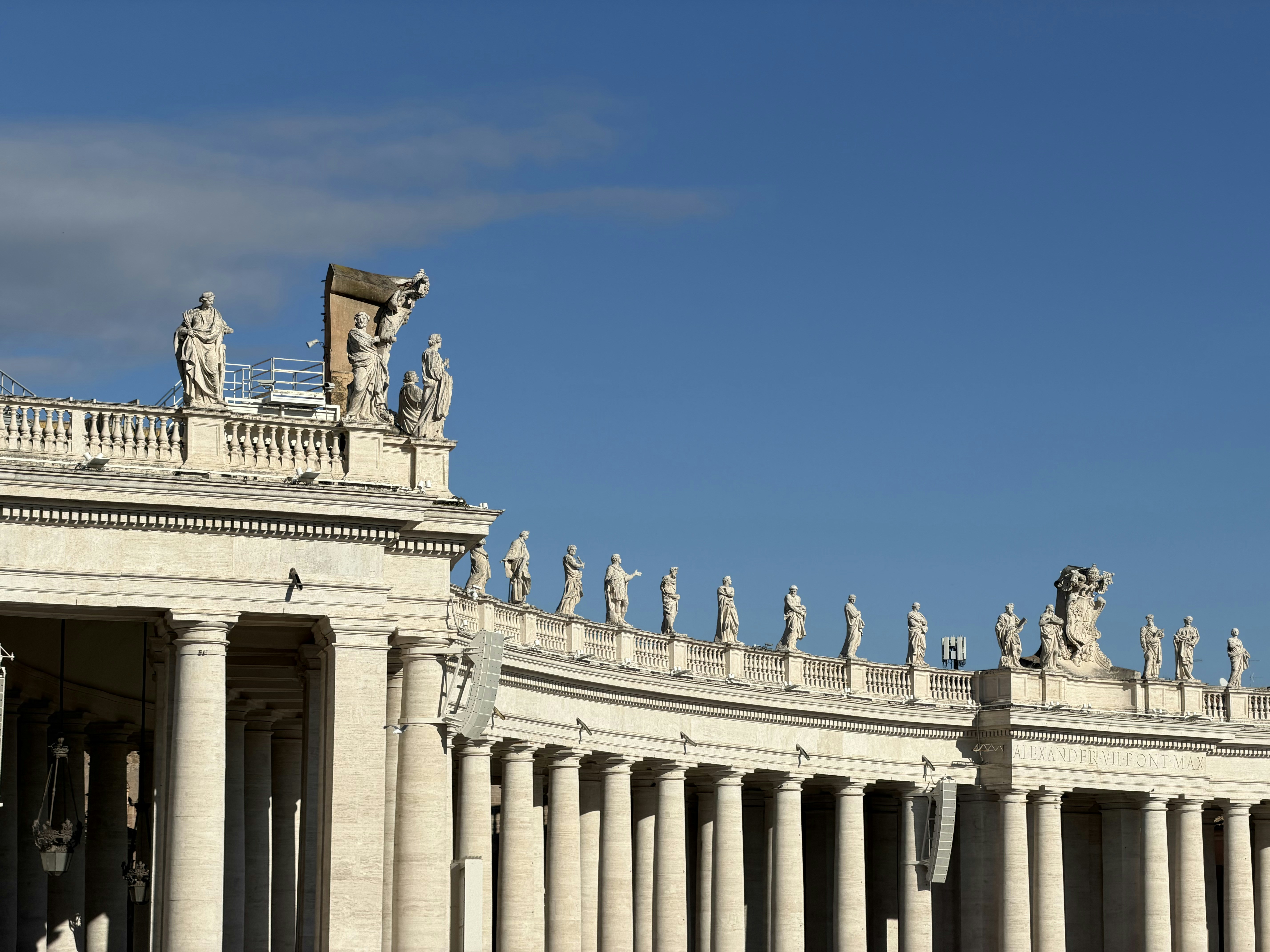 Statues line the colonnade under a clear blue sky.