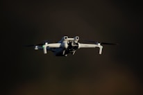 A white drone flying against a dark background