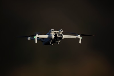 A white drone flying against a dark background