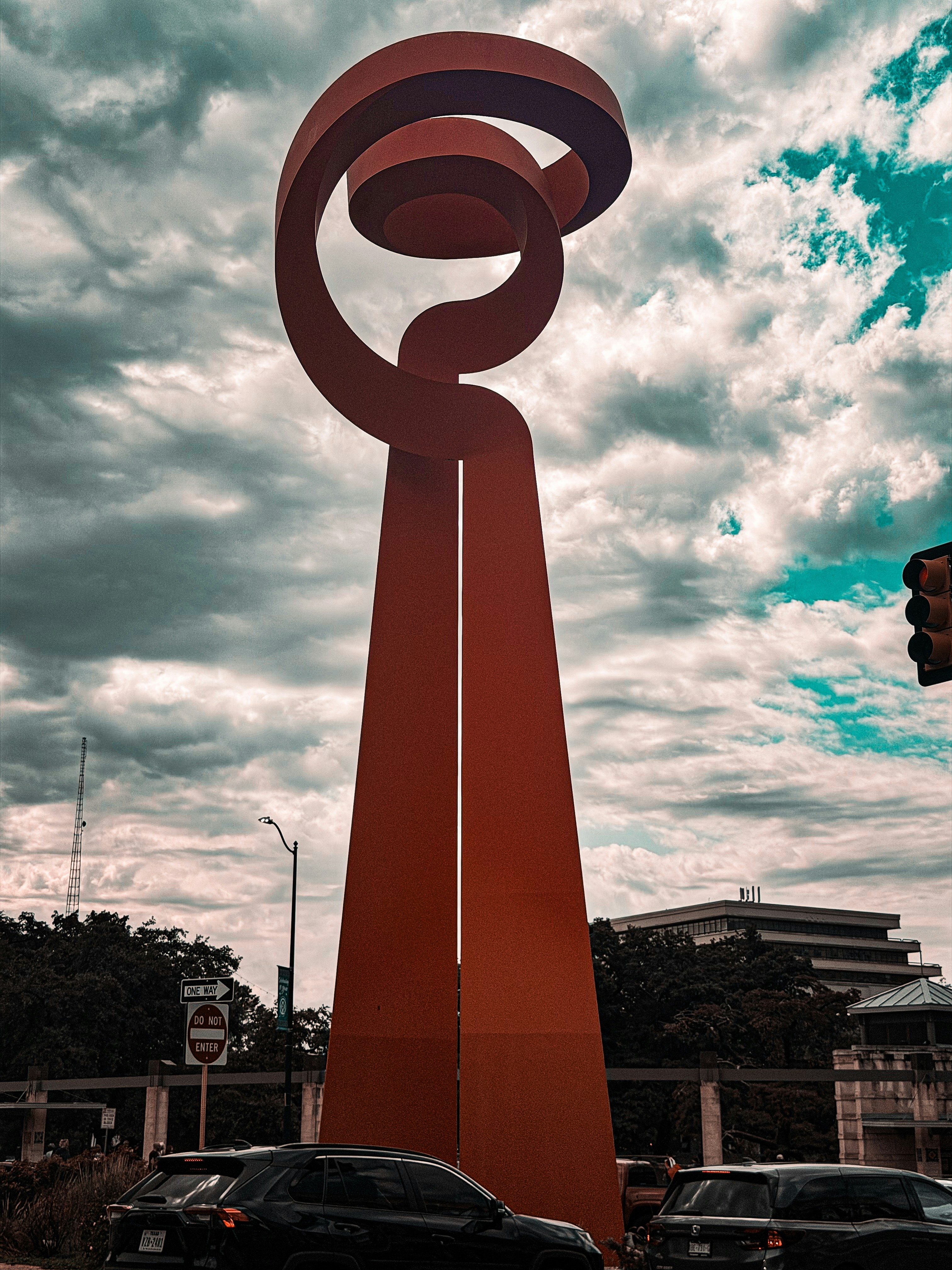 Tall red abstract sculpture against cloudy sky