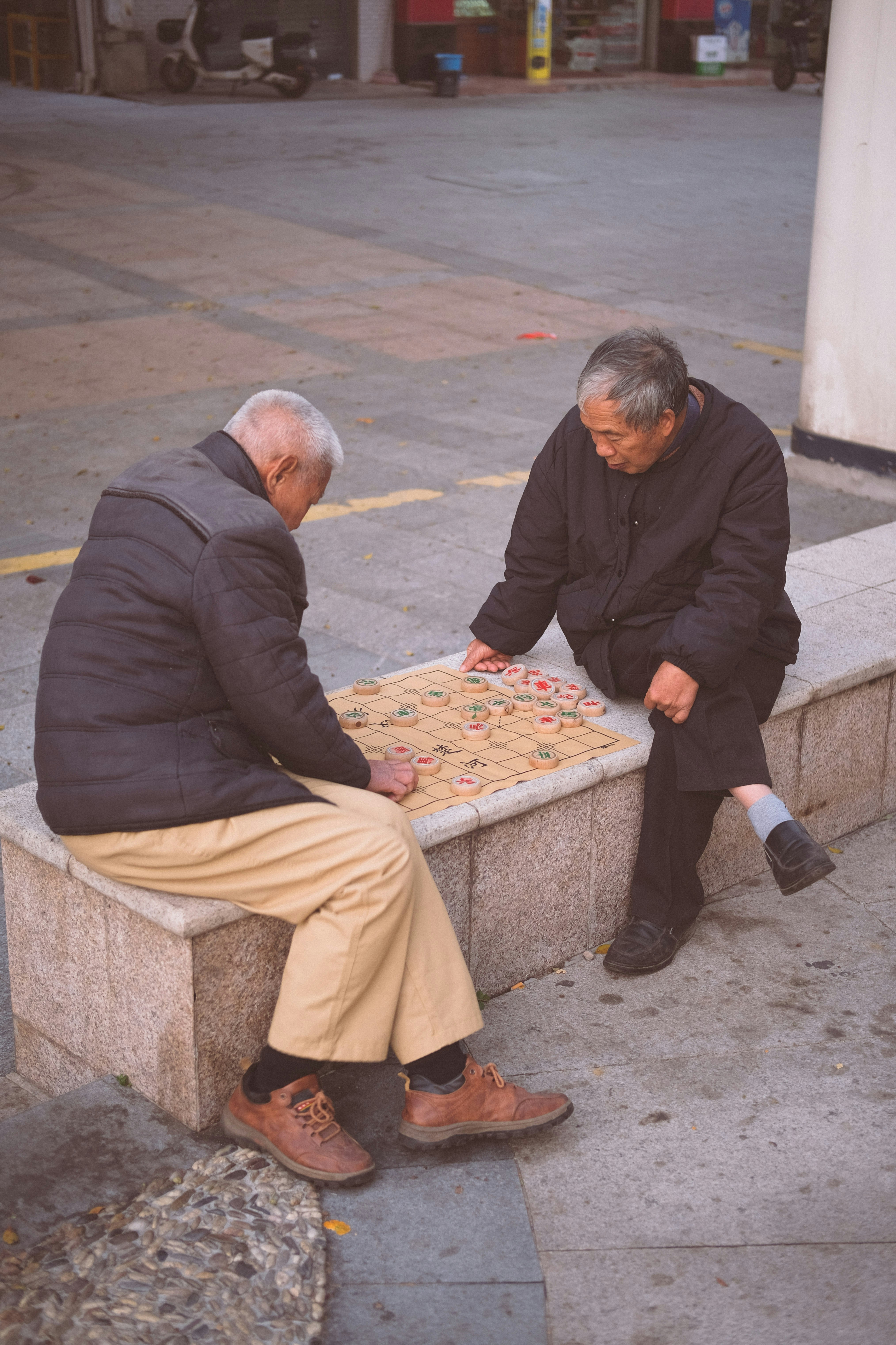 Two elderly men playing a board game outdoors.