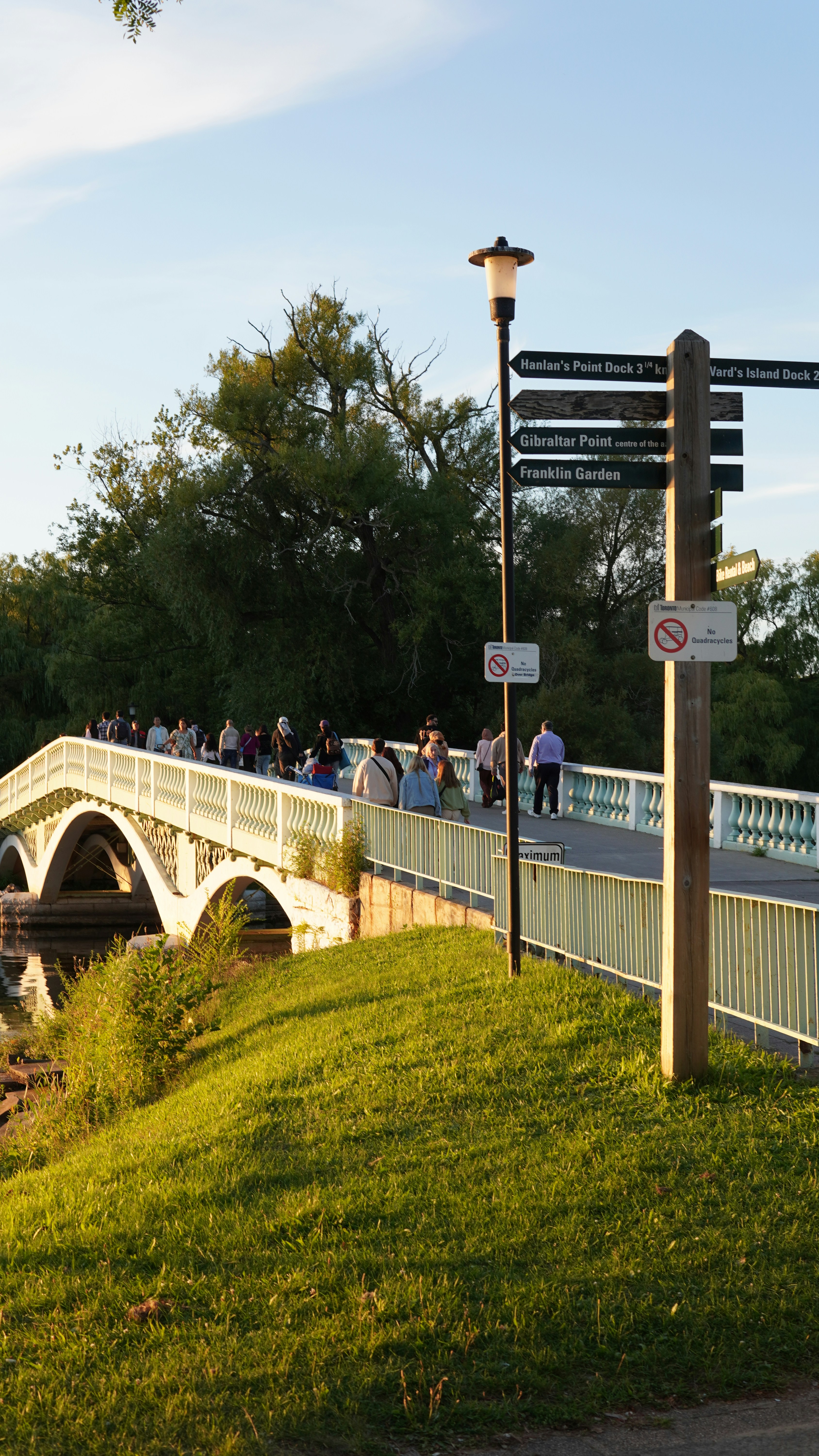 People walk across a bridge with a signpost.