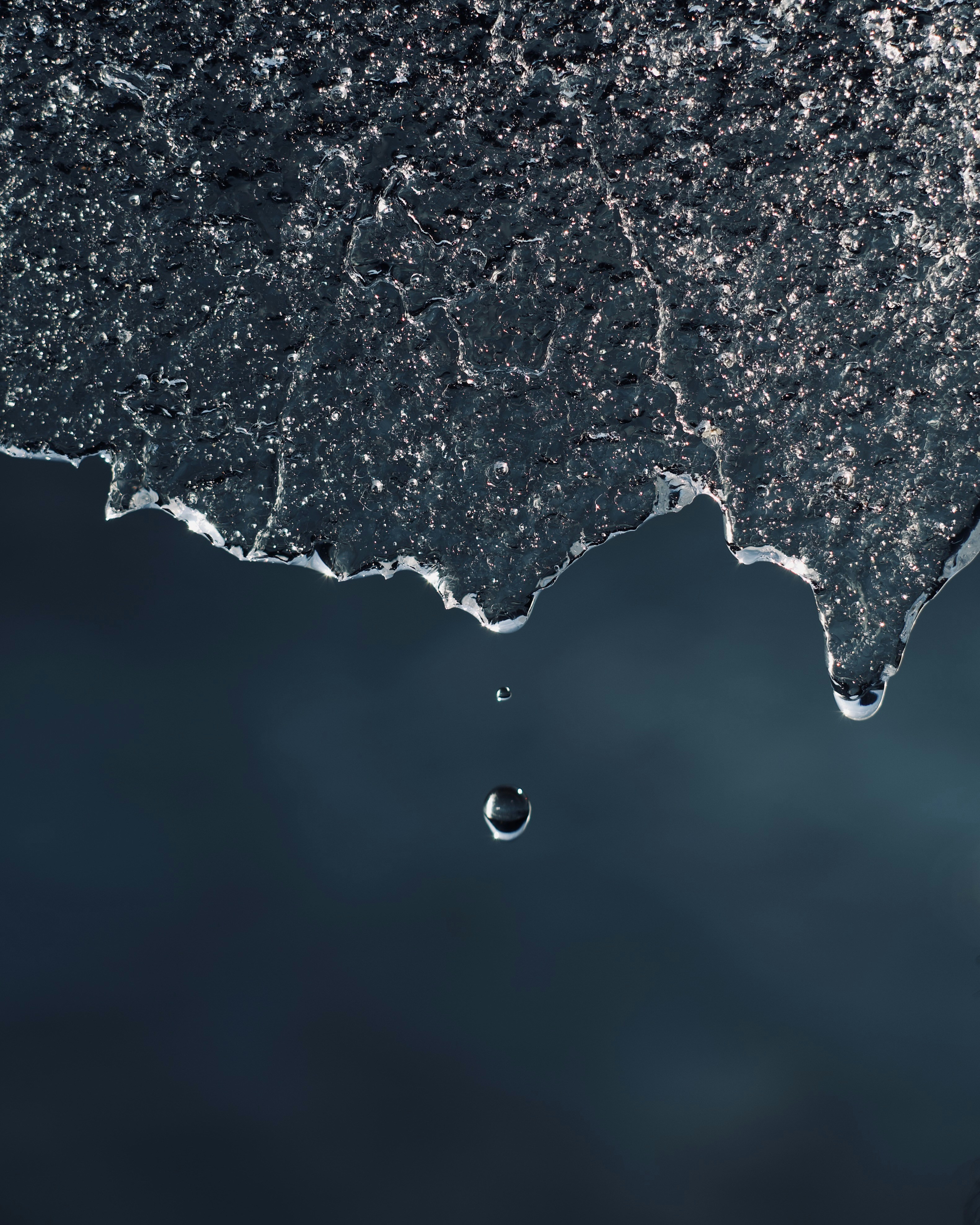 A water droplet falls from melting ice.