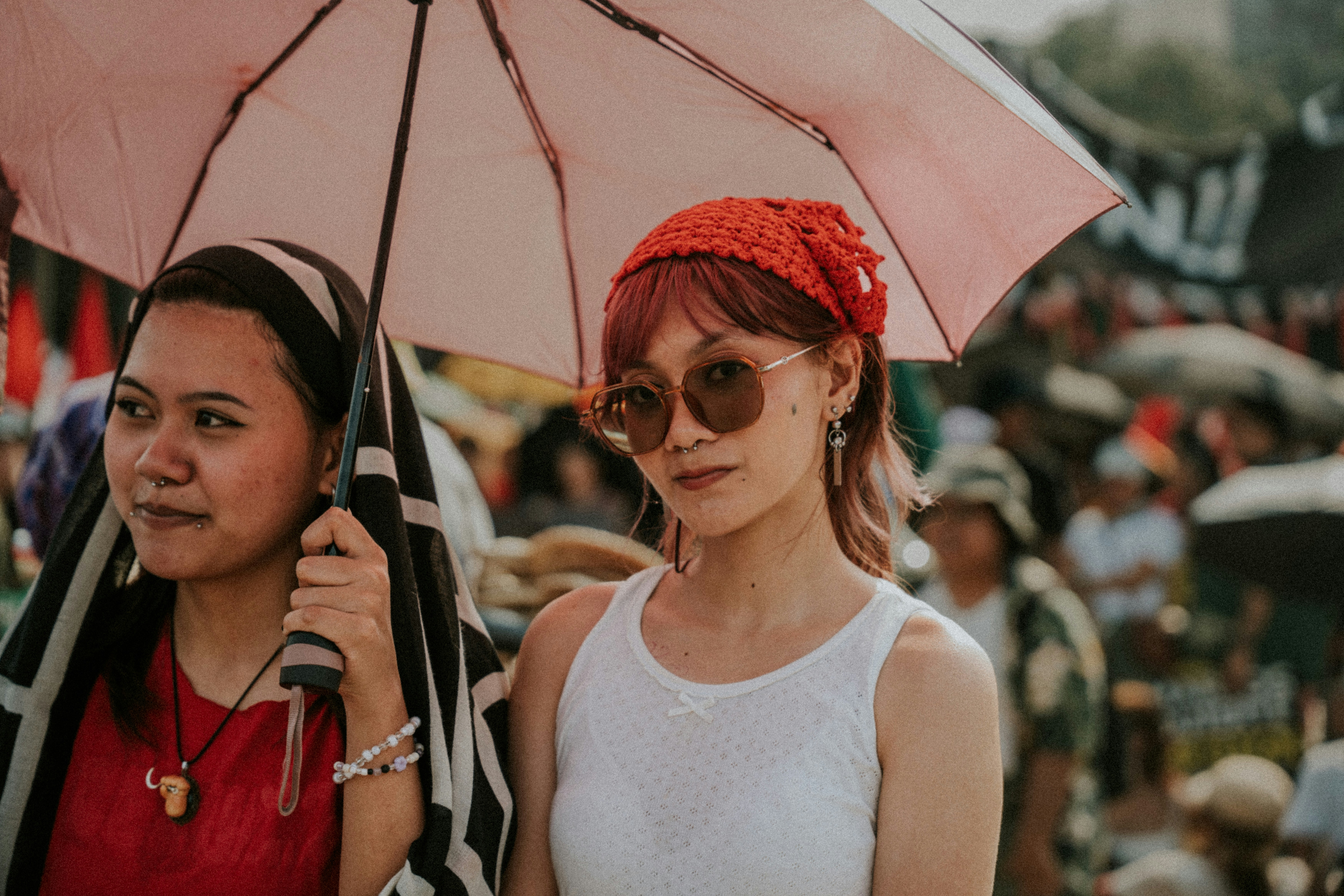 Two women under a pink umbrella in a crowd.