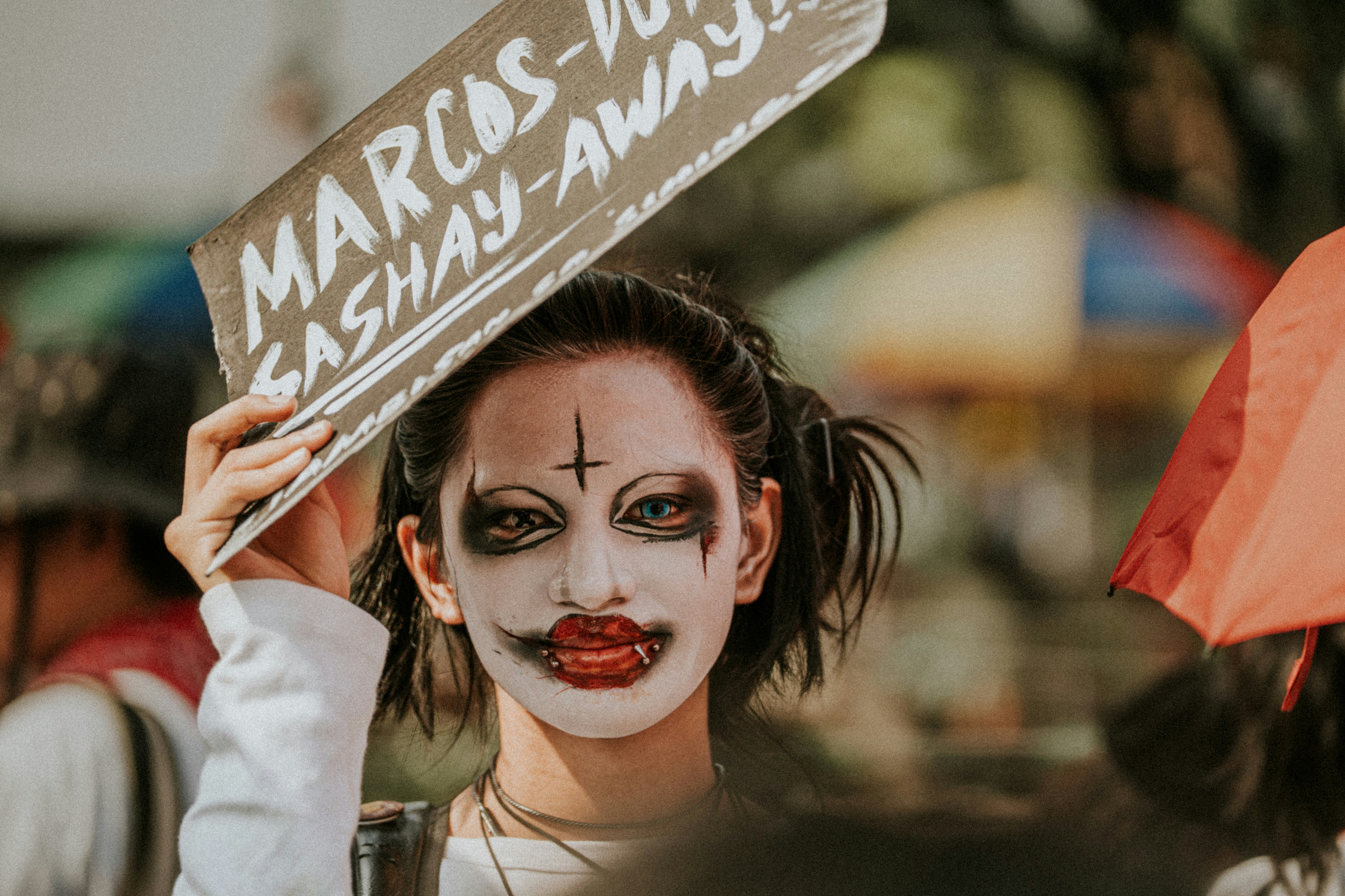 Person with clown makeup holds protest sign