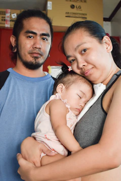 A mother holds her sleeping baby while father stands beside.