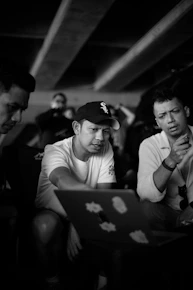 Three men gathered around a laptop computer.