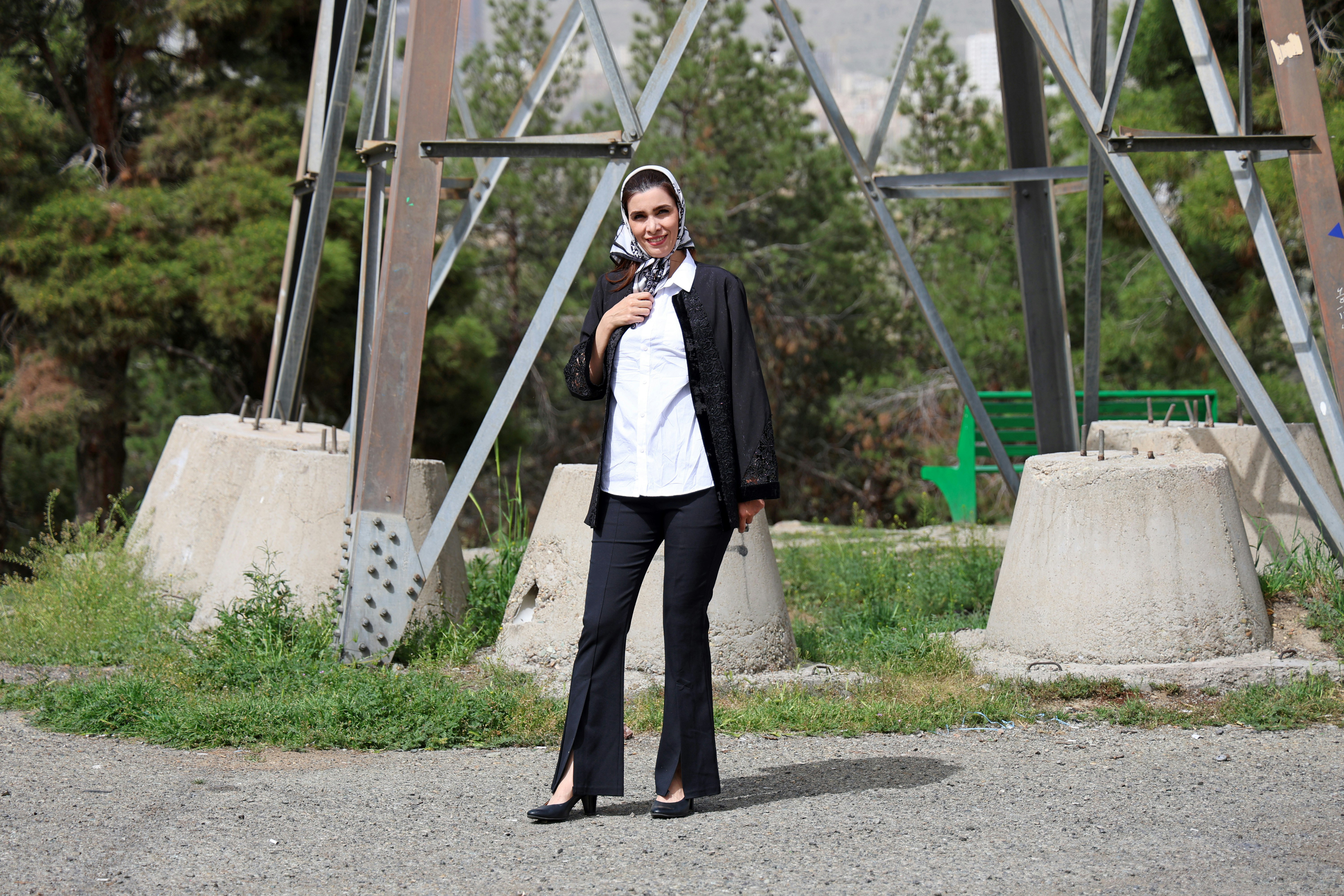Woman in black jacket and white shirt poses near tower.