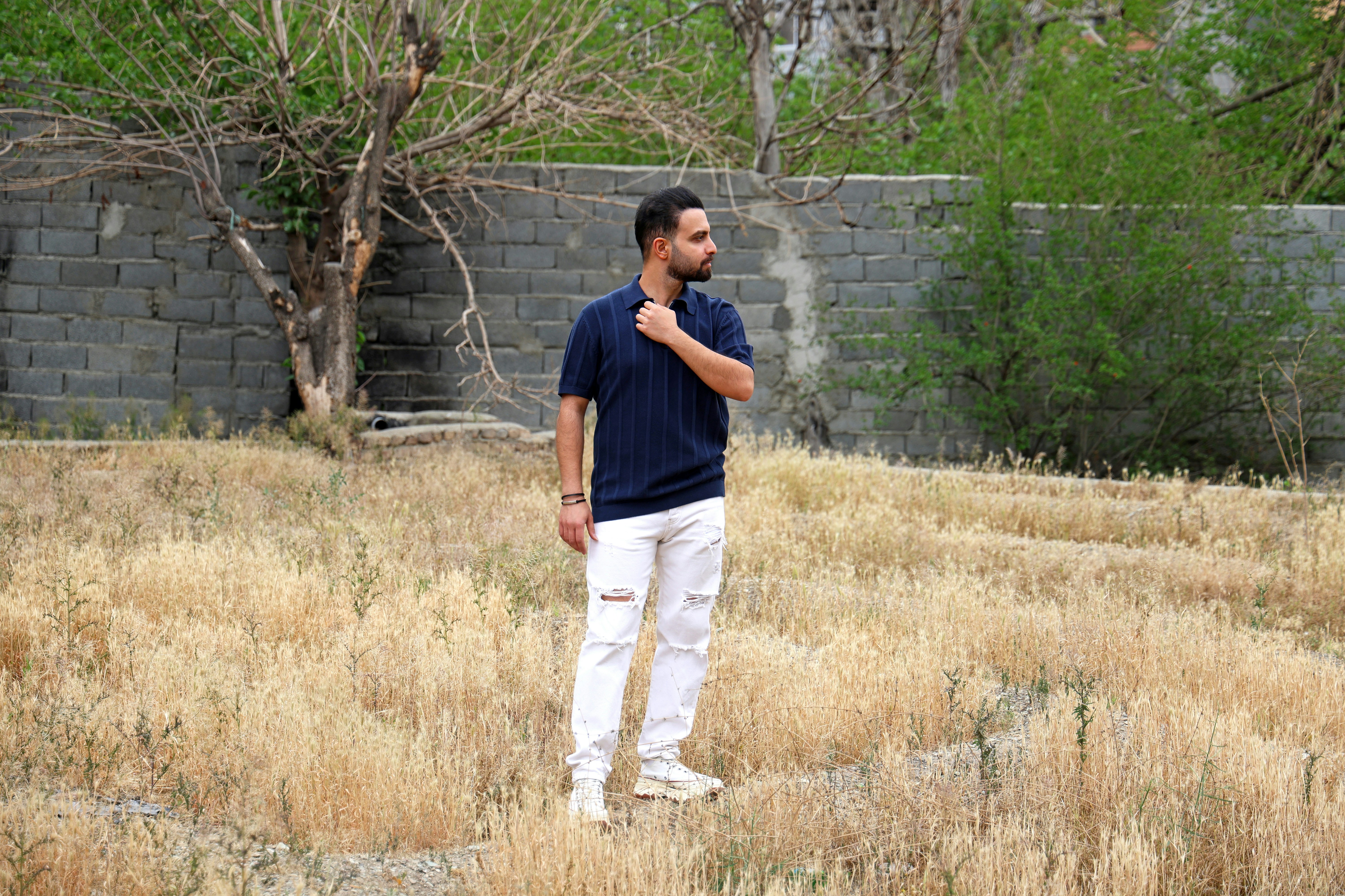 Man standing in dry grass near stone wall
