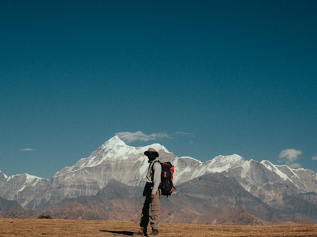 Hiker with backpack stands before snowy mountain range.